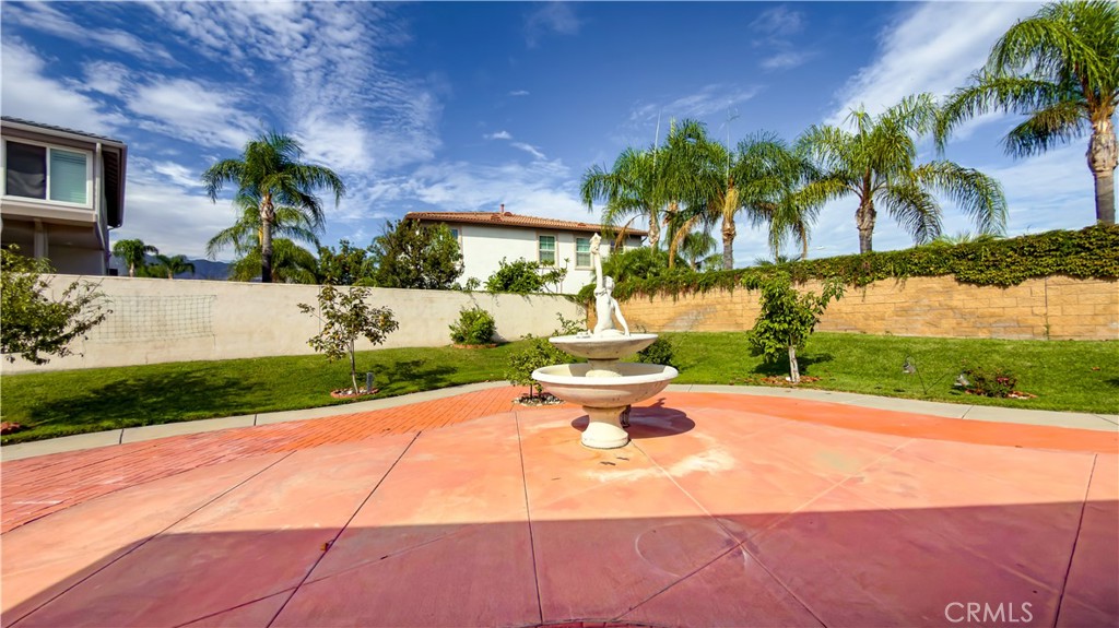 Backyard patio with a tiered fountain, green lawn, and palm trees.
