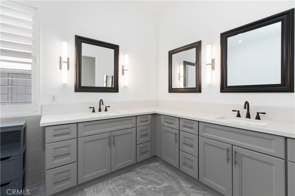 Bathroom with an L-shaped double vanity, gray cabinetry, framed mirrors, and black faucets.