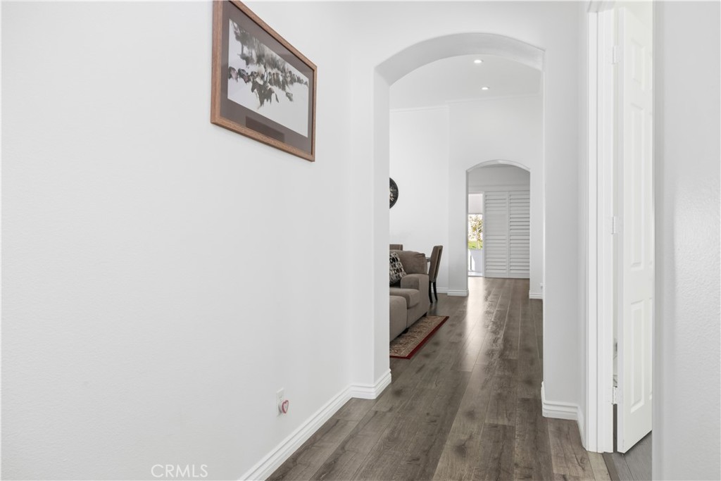 Hallway with gray wood-look floors, arched openings, and a glimpse of a living room sofa.