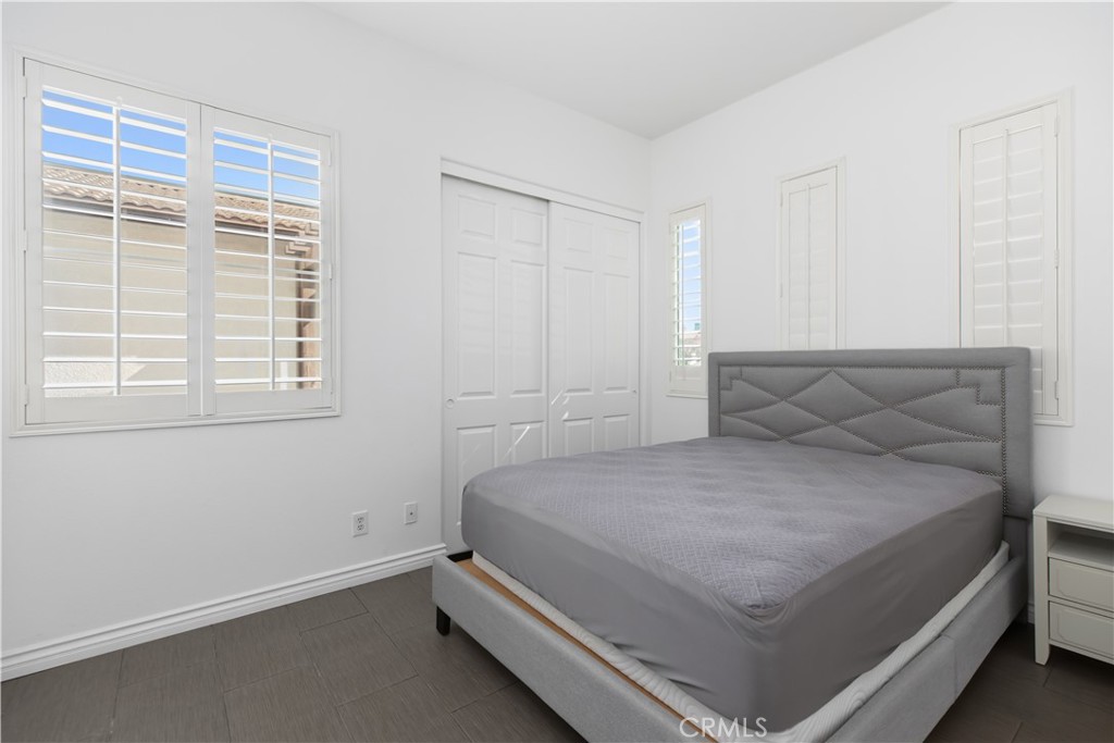 Bedroom with a gray upholstered bed, white plantation shutters, and dark wood-look flooring.