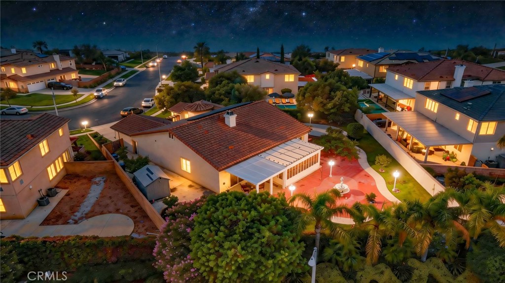 Aerial view of a tiled-roof home, enclosed yard, and illuminated patio at night.