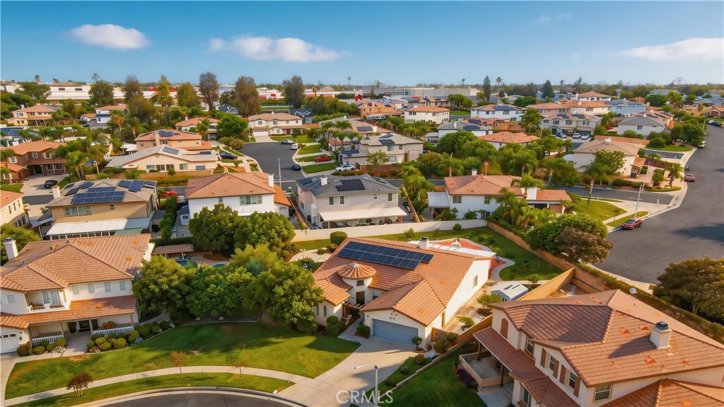 Aerial view of a suburban neighborhood with tile-roof homes, landscaped yards, and rooftop solar panels.
