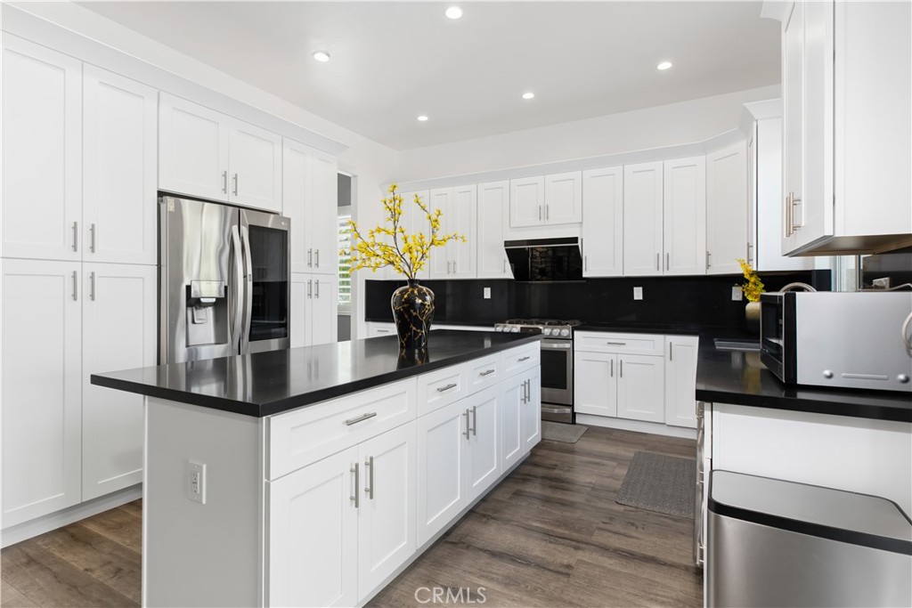 Kitchen with white cabinets, black countertops, a large island, stainless steel appliances, and wood-look flooring.