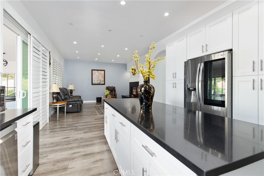 Kitchen with a large dark island, white cabinetry, and stainless steel appliances opening to a living area.