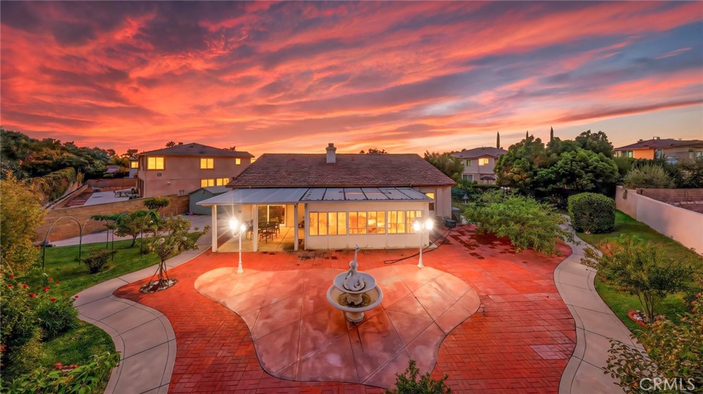 Rear of a house with a curved brick patio, central fountain, and sunset-lit windows.