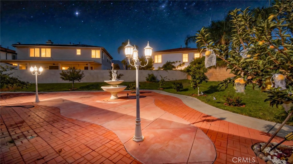Paved courtyard with a tiered fountain and decorative lamps at night, with the home in the background.