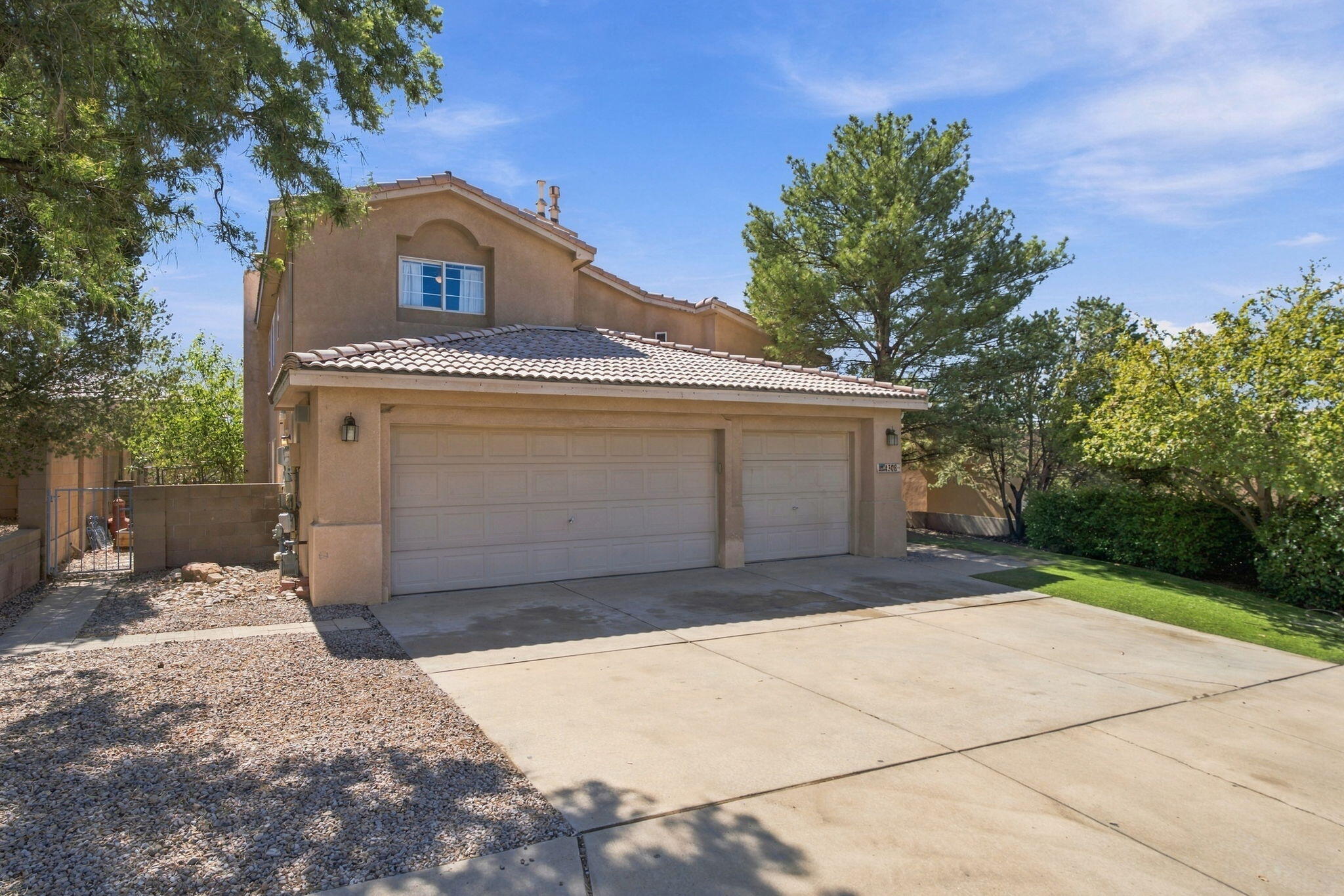 Two-story tan stucco home with a tiled roof, three-car garage, and broad driveway.