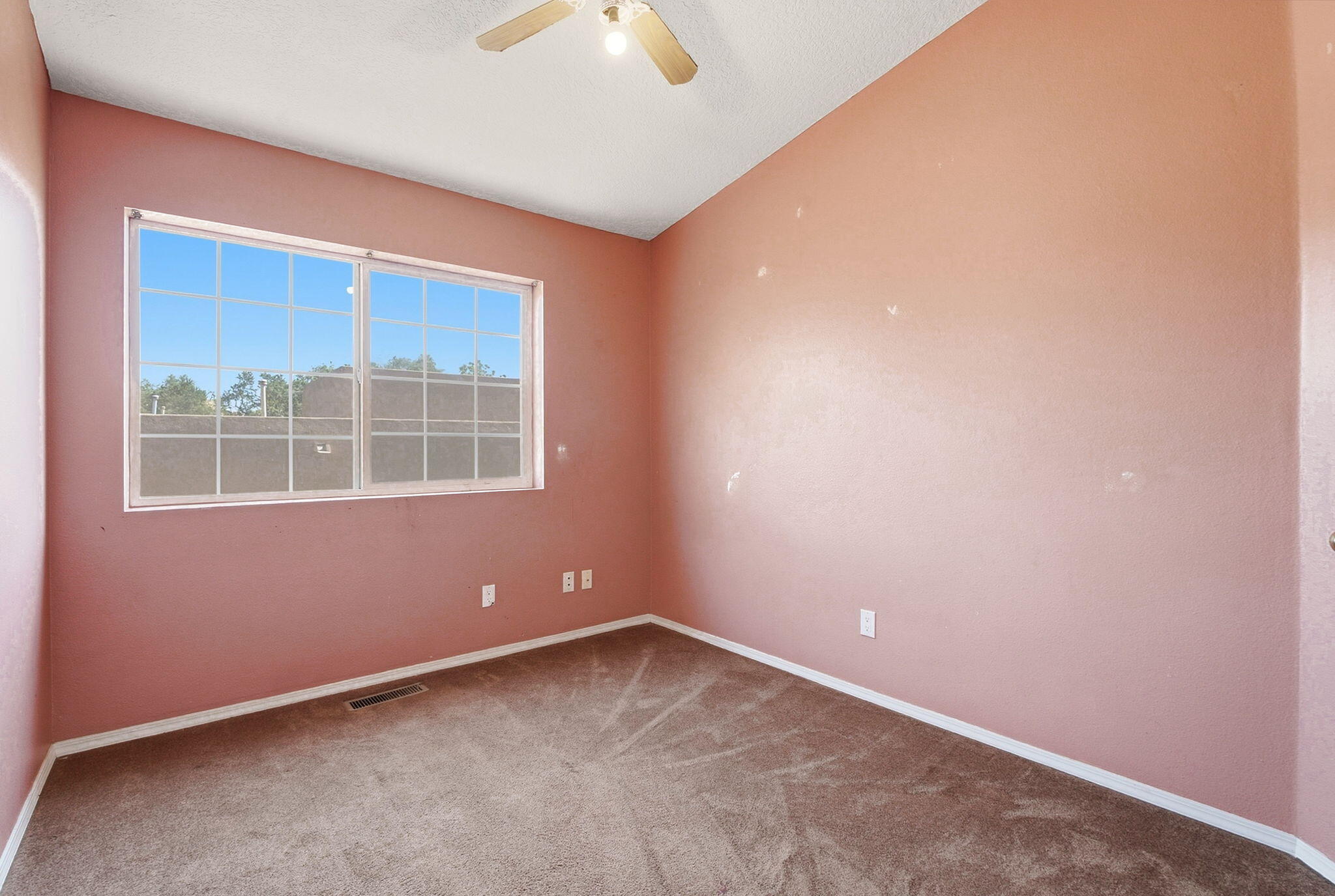Empty bedroom with rose-colored walls, carpet, and a large window.