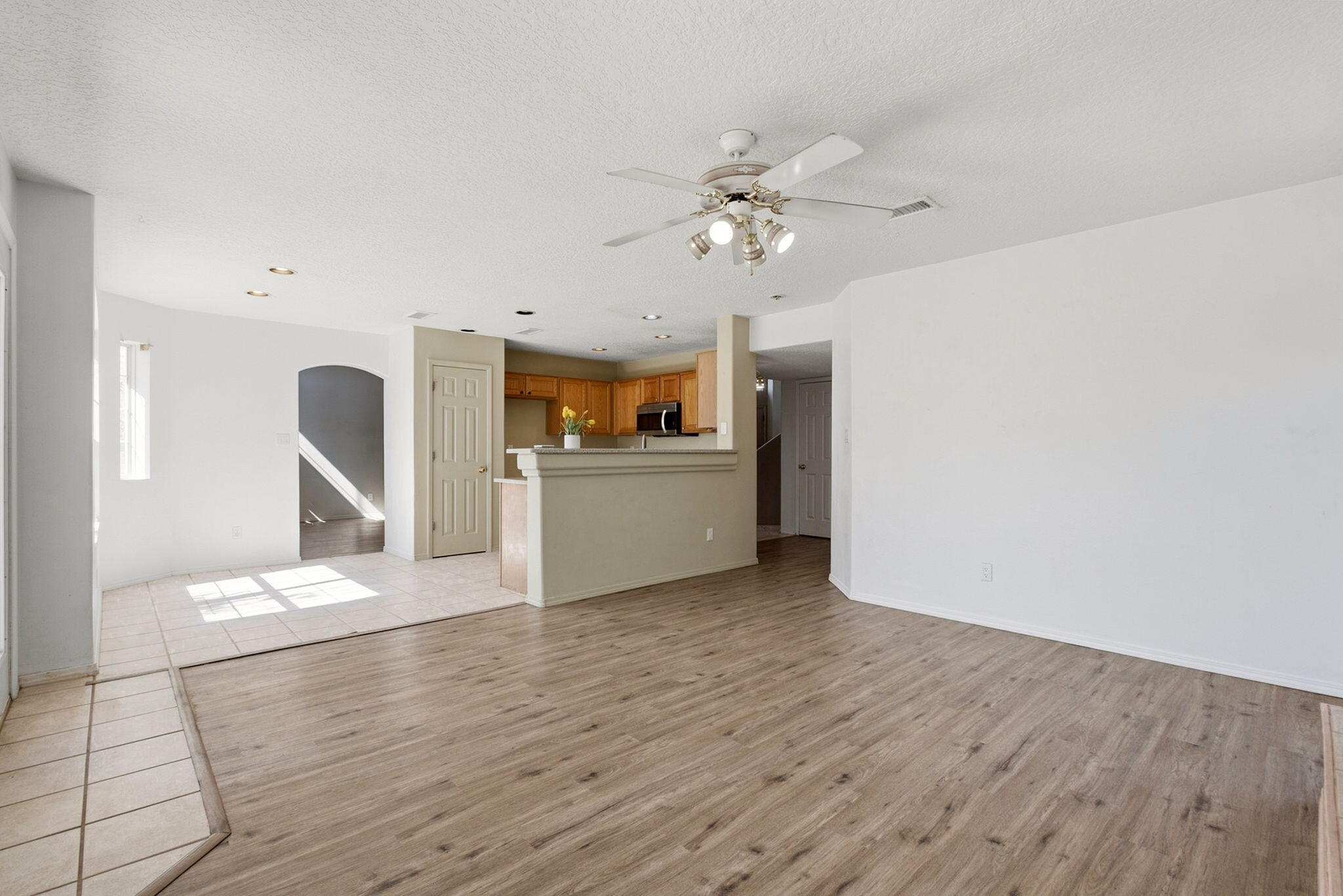 Unfurnished living area with wood-look floors, tiled dining space, kitchen breakfast bar, and ceiling fan.