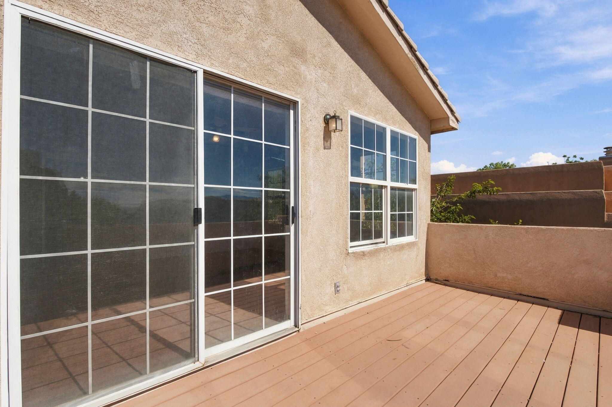 Raised deck with tan plank flooring, sliding glass door, and stucco privacy wall.