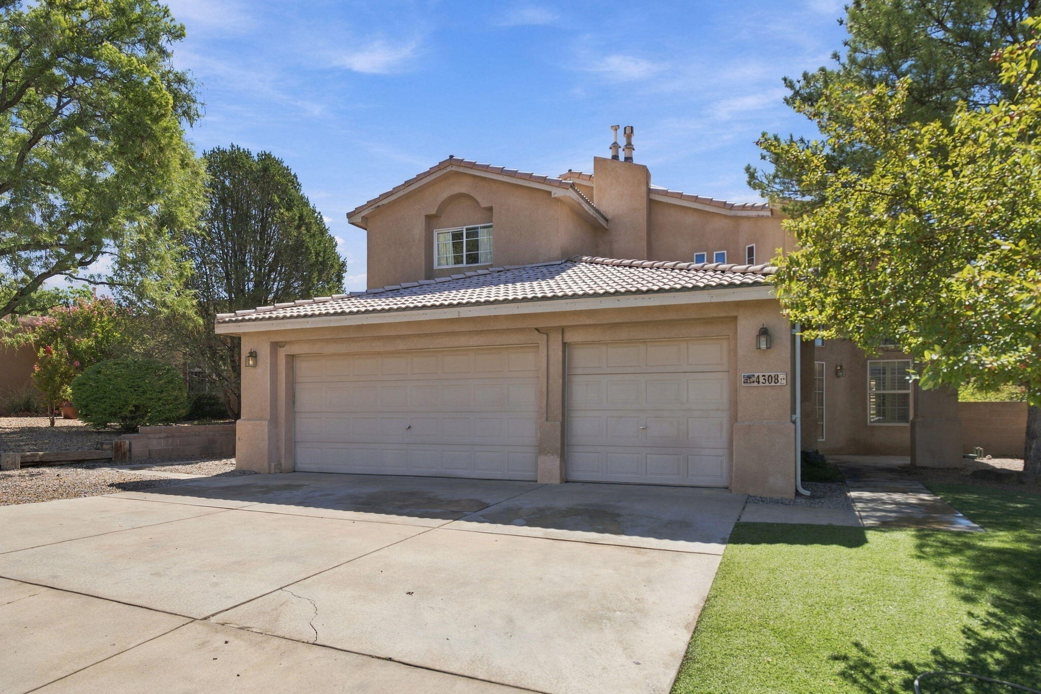 Two-story stucco home with a tiled roof, double garage, broad driveway, and mature trees.