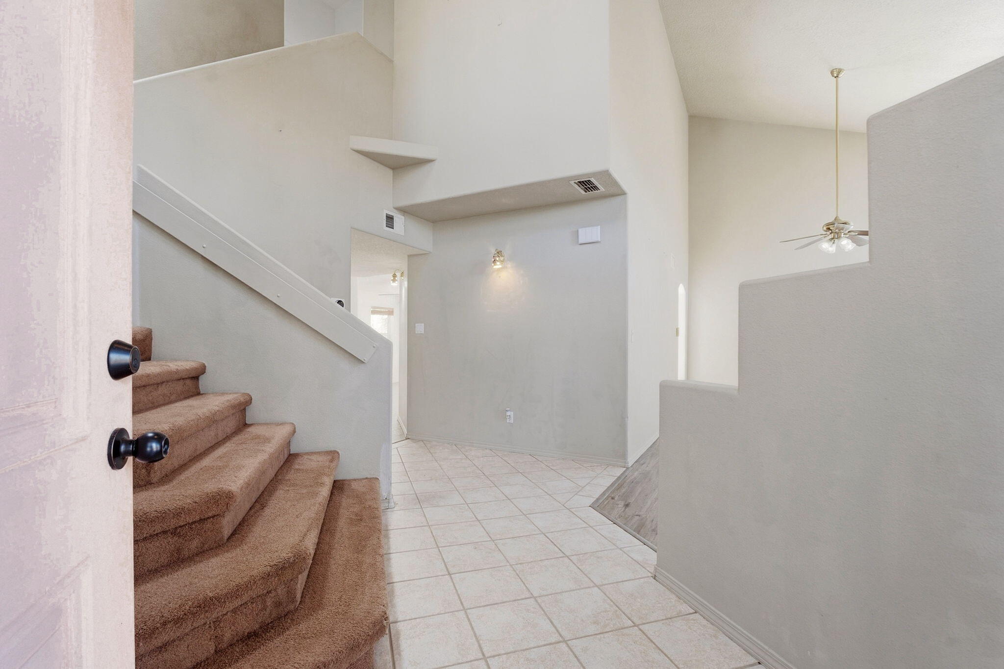 Vacant entryway with carpeted stairs, light tile flooring, and a view into the adjoining room.