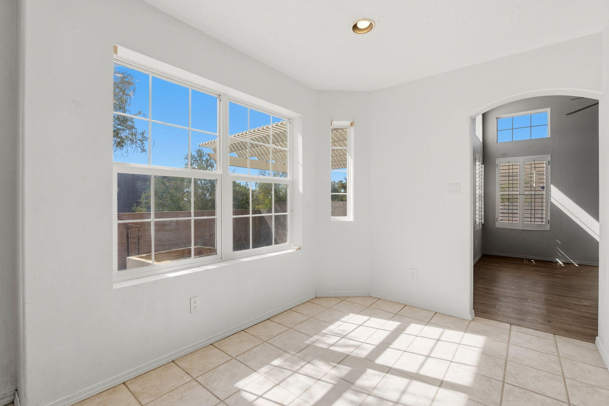 Bright tiled room with large windows and an arched opening to a wood-floored adjoining room.