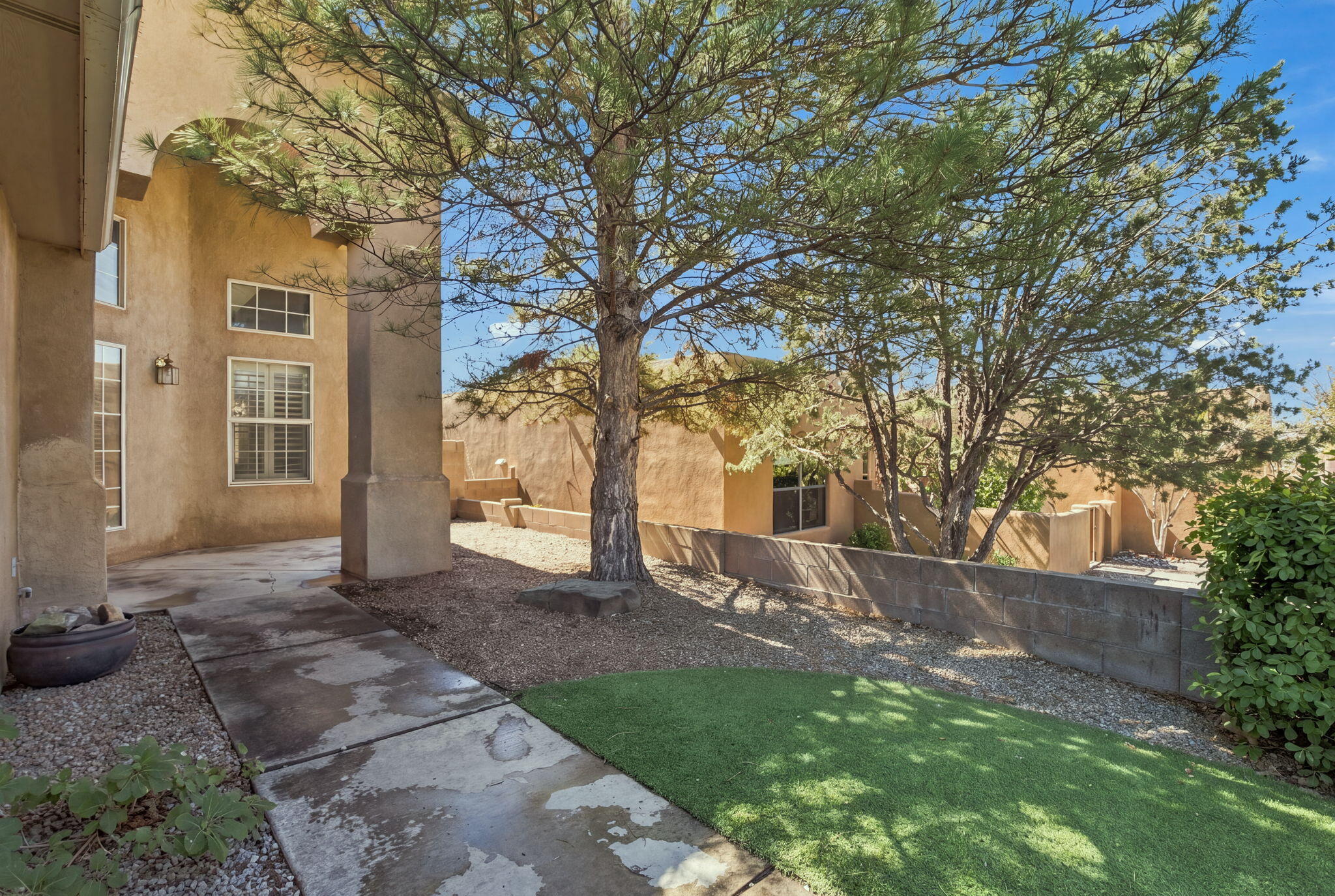 Backyard patio with a concrete walkway, artificial-turf lawn, gravel beds, and mature shade trees.