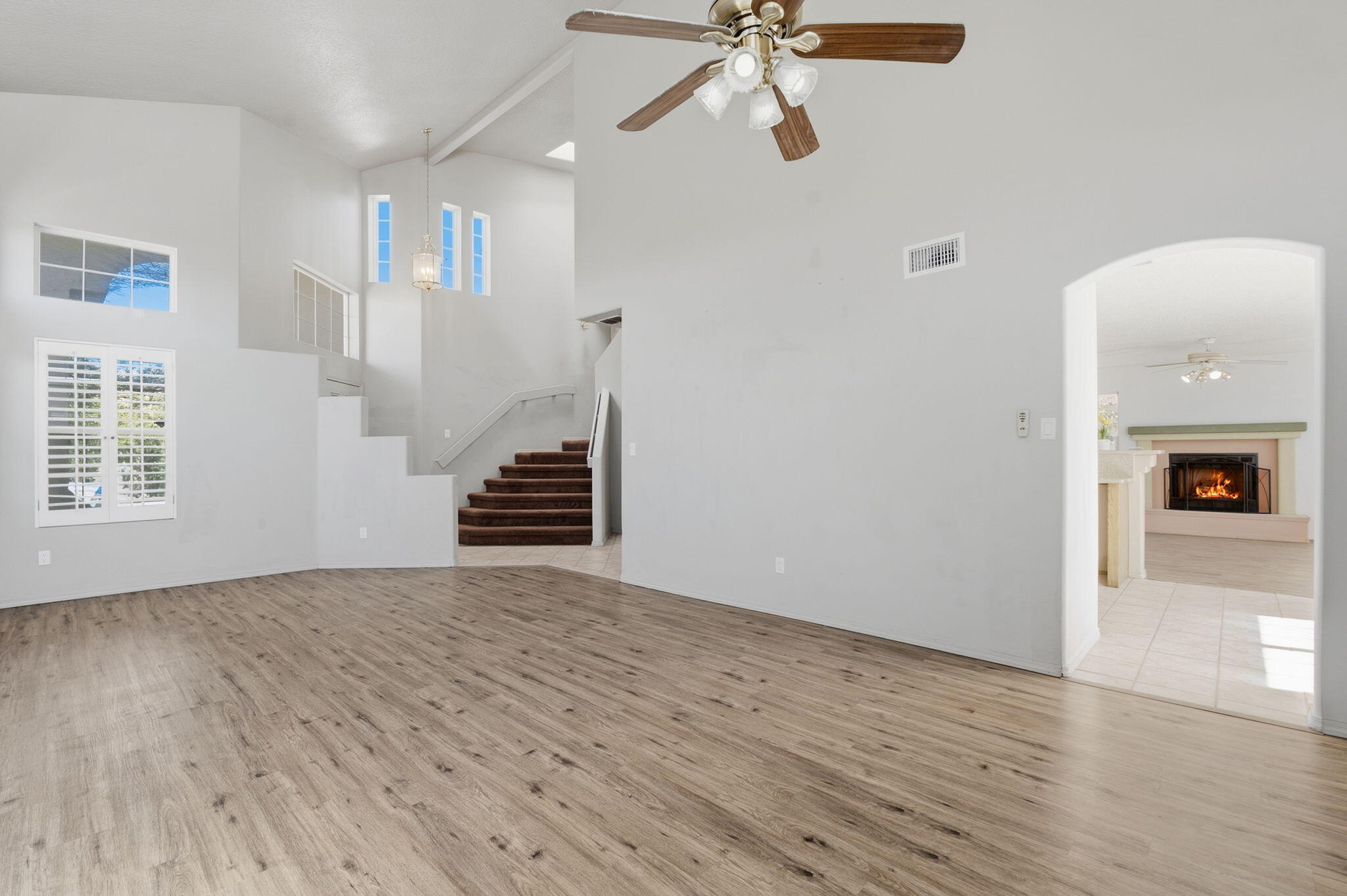 Empty living room with wood-look floors, a tall ceiling, staircase, and arched view of a lit fireplace.
