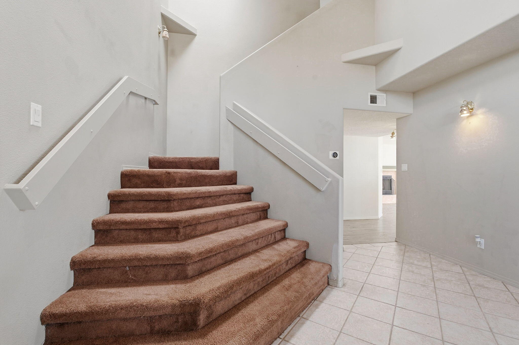 Curved brown carpeted staircase with white handrails beside the tiled entryway.