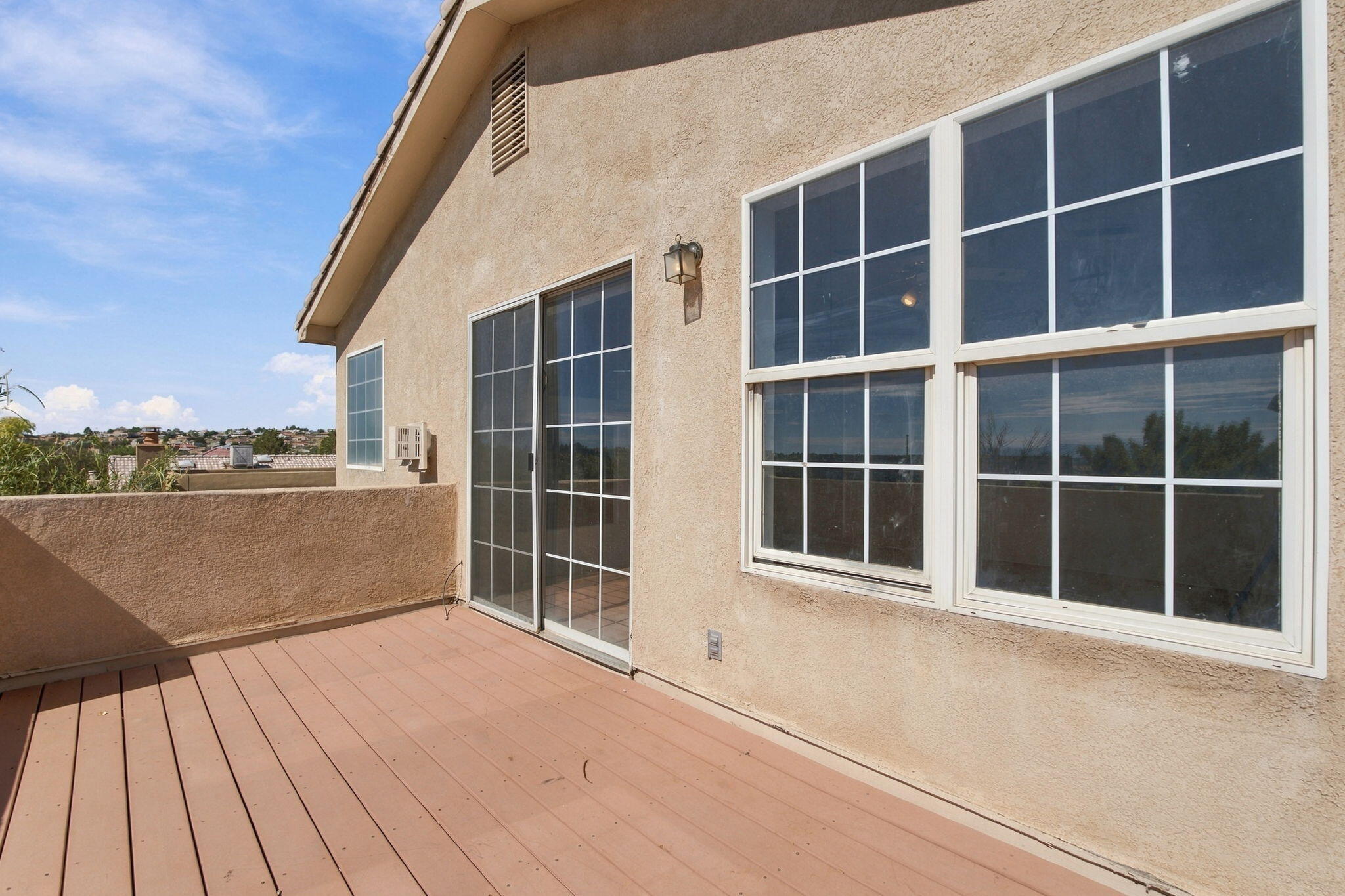 Raised composite deck beside a stucco home, with sliding glass doors and large grid-pane windows.