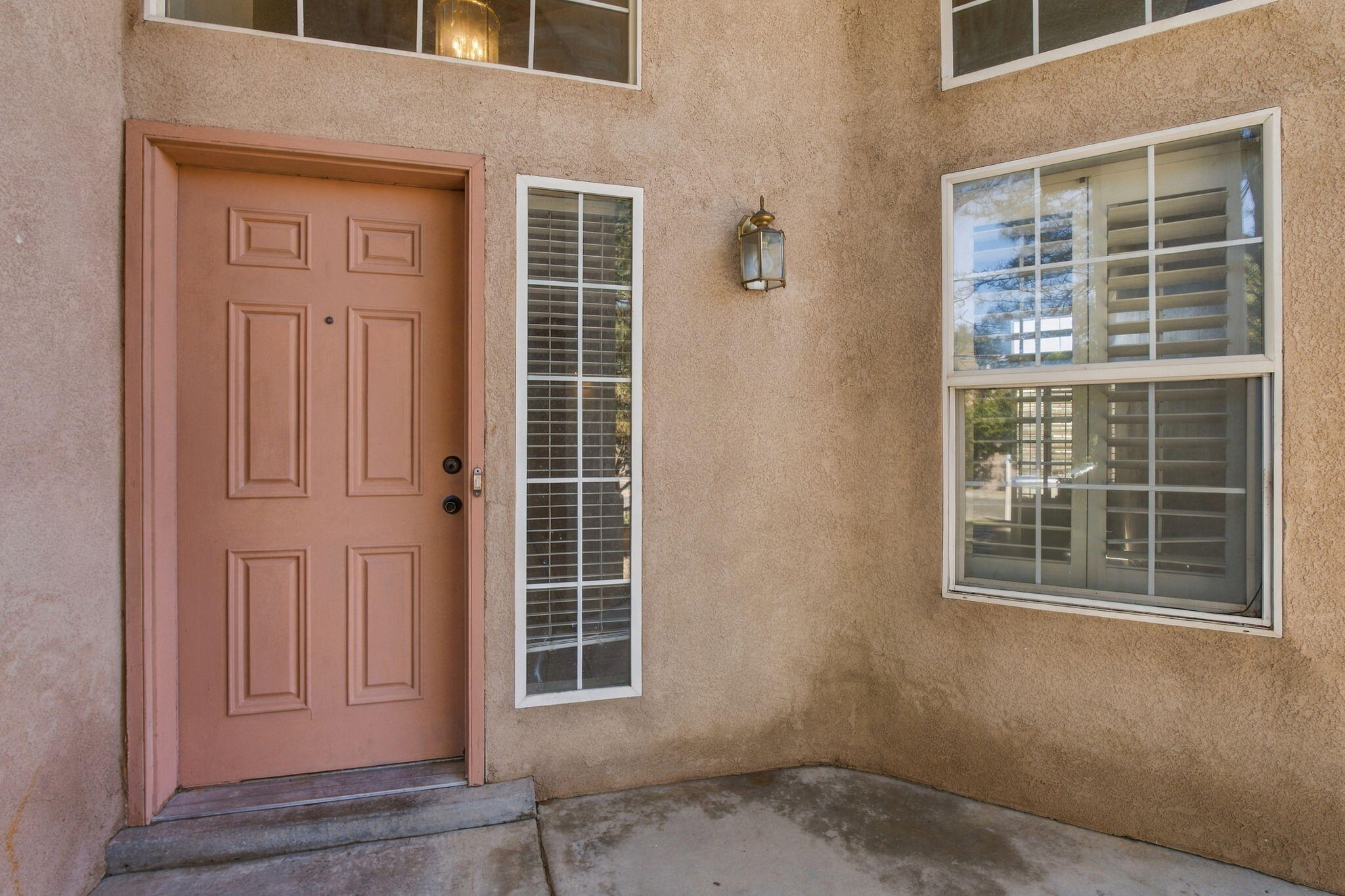 Home entrance with a terracotta paneled door, tan stucco, shuttered windows, and a wall lantern.