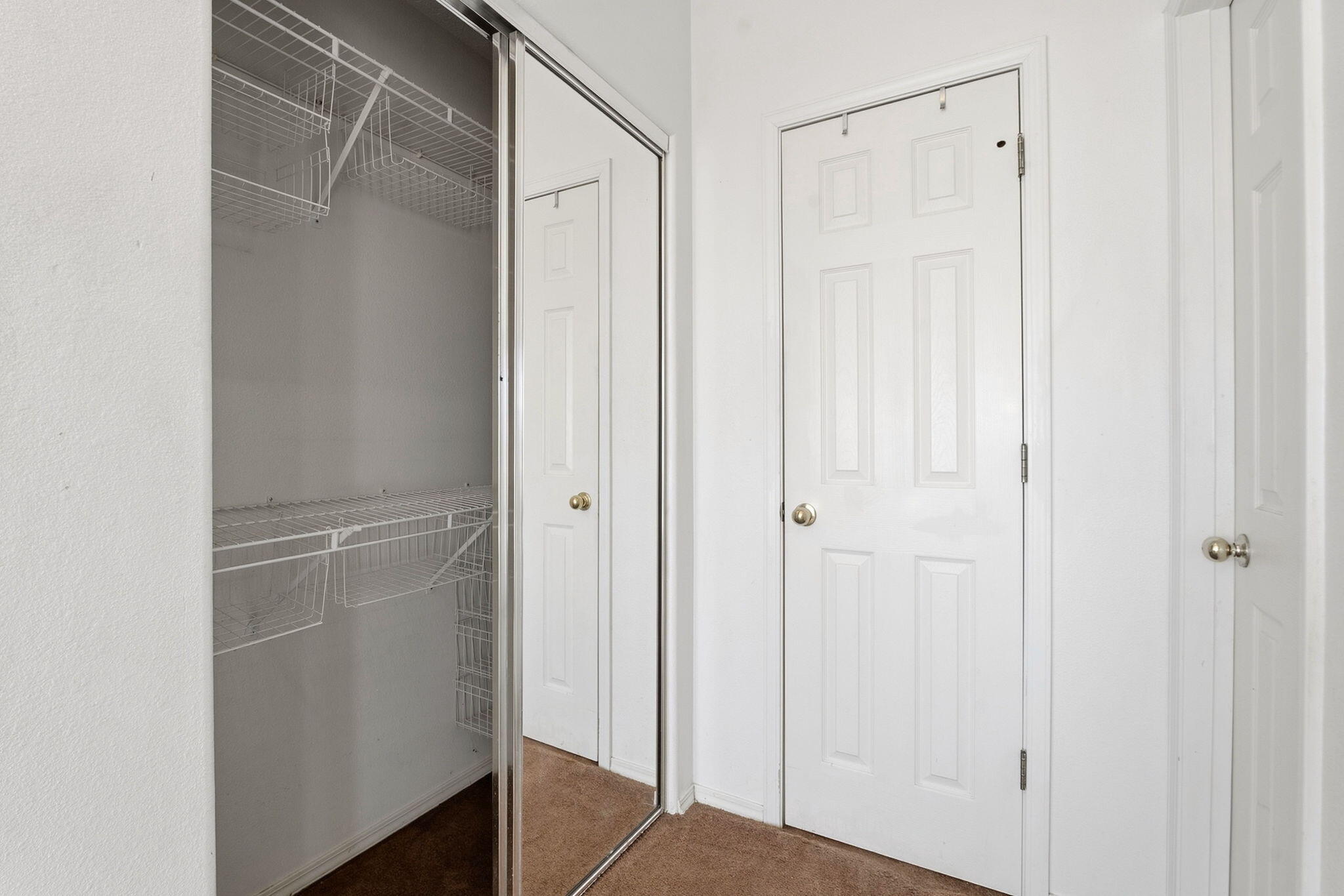 Bedroom closet with white wire shelving, mirrored sliding doors, and brown carpet.