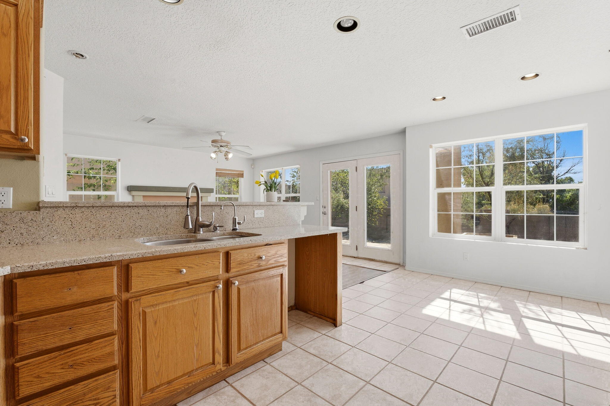 Kitchen with oak cabinets and speckled counters, opening to a sunny tiled dining area with French doors.