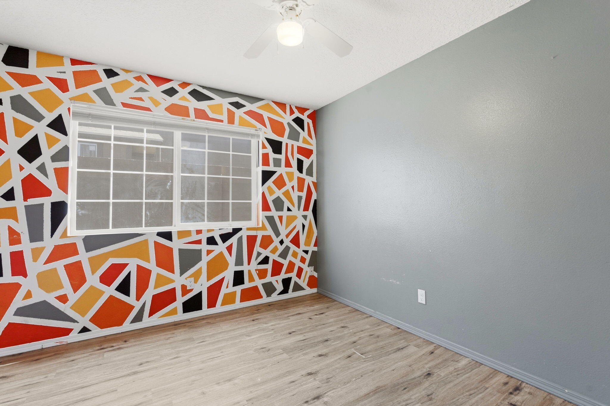 Vacant room with a colorful geometric accent wall, window, and wood-look flooring.