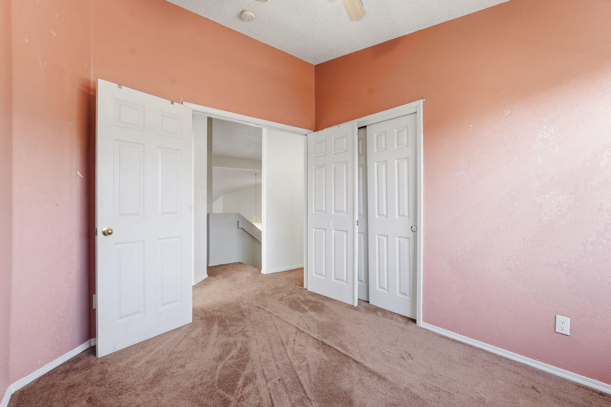 Empty bedroom with pink walls, brown carpet, and open white closet doors.