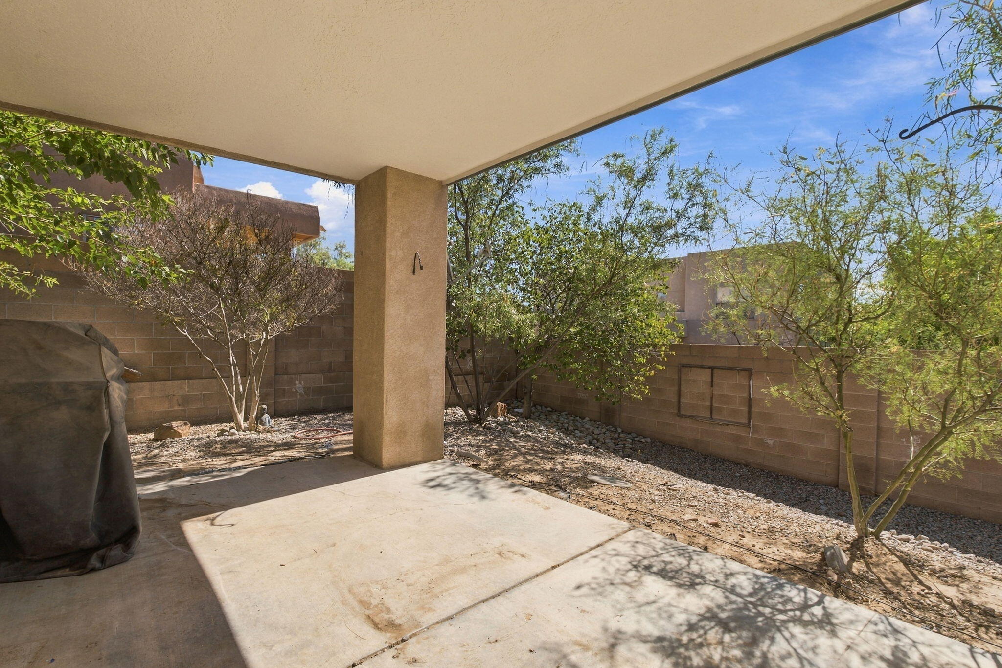 Covered patio overlooking a gravel backyard with leafy trees and a block wall.