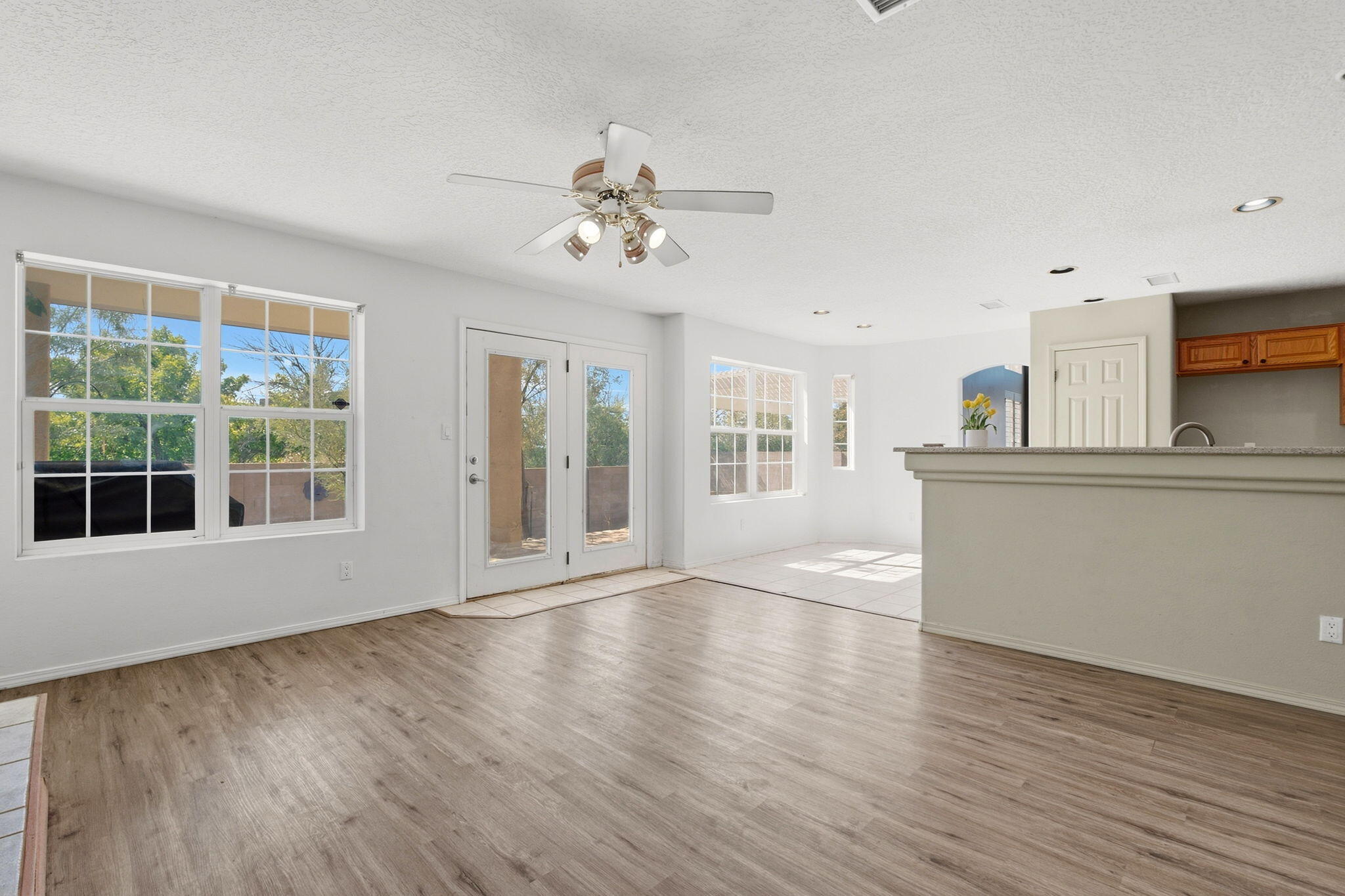 Unfurnished living area with wood-look floors, large windows, patio doors, and a kitchen breakfast bar.