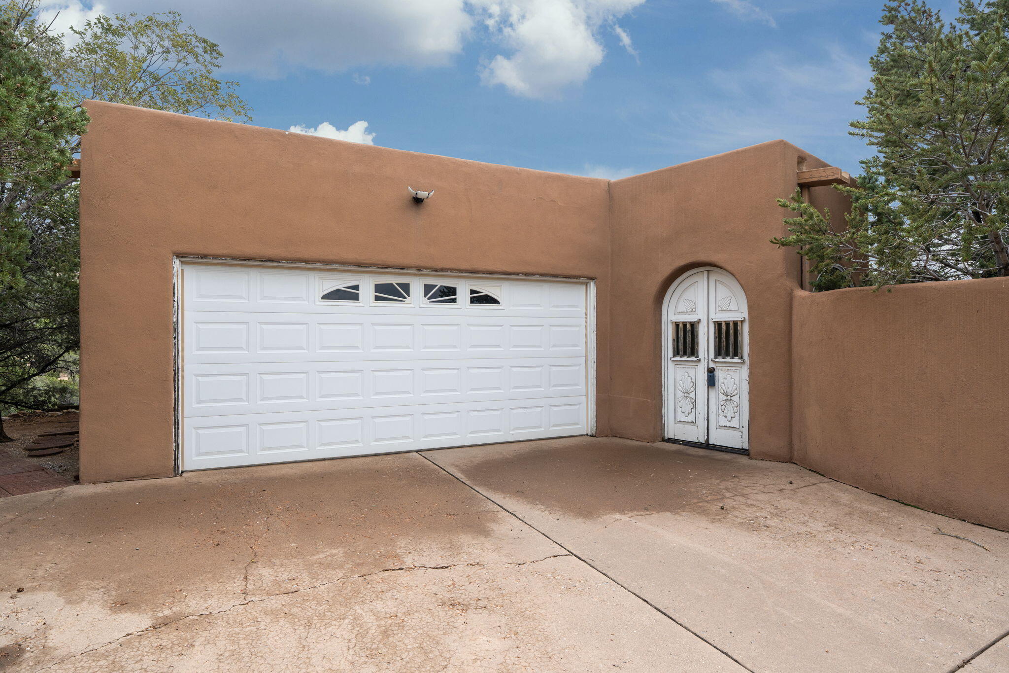 Tan stucco home with a wide white garage door and ornate arched entry doors.