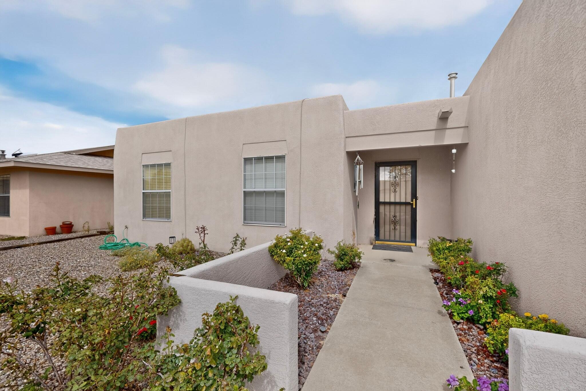 Stucco home entry with a barred door, concrete walkway, and flowering gravel landscaping.