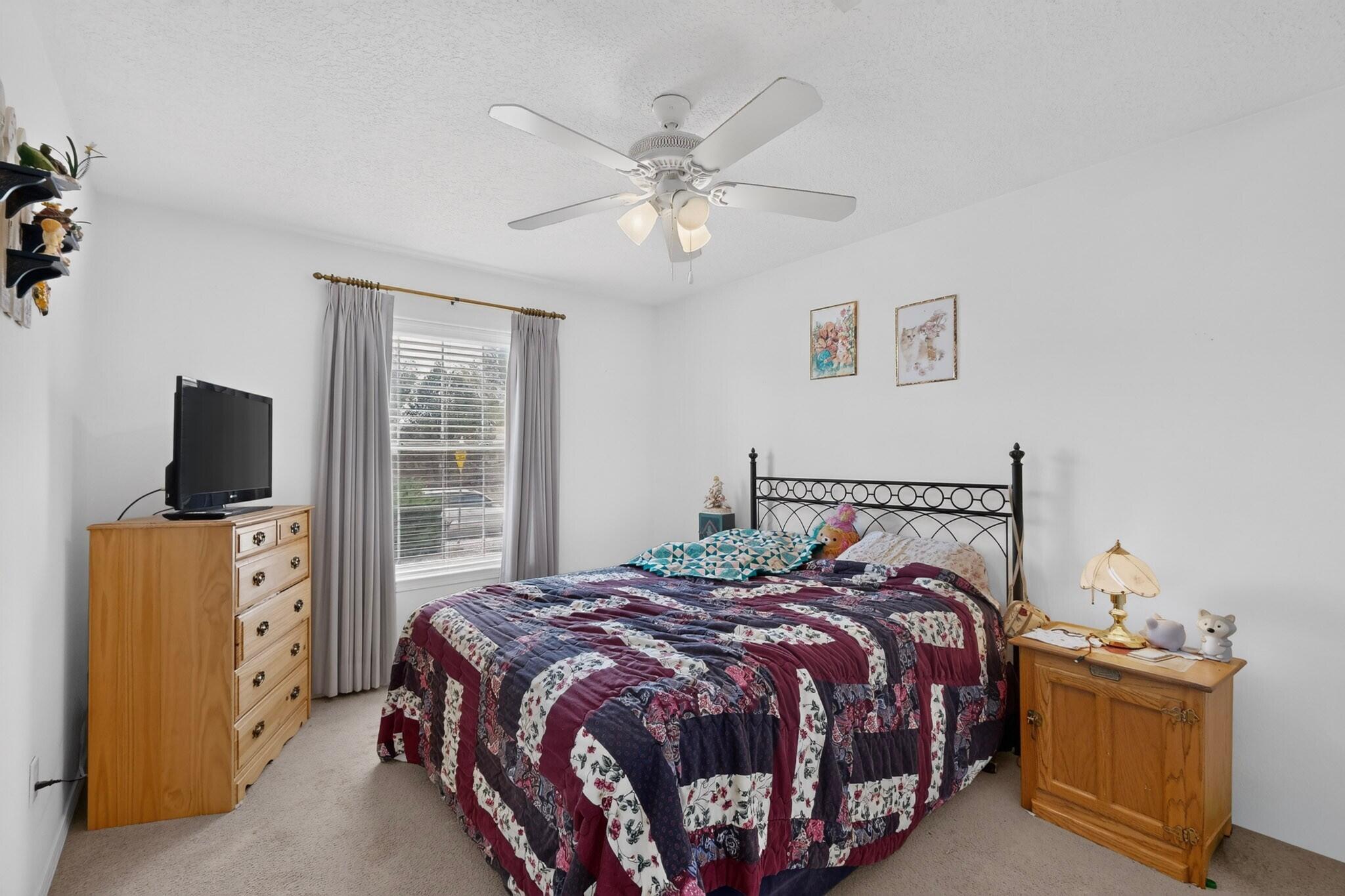 Furnished bedroom with a colorful patchwork quilt, black metal bed frame, and wooden furniture.