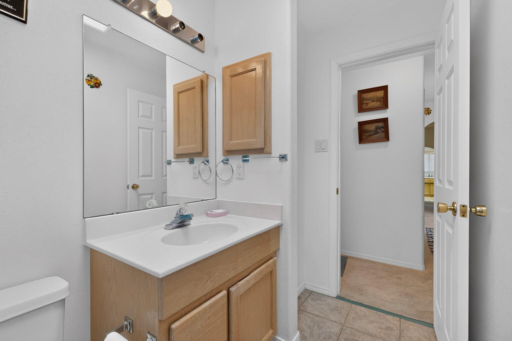 Bathroom with a light wood vanity, white sink, large mirror, and open doorway to a carpeted room.