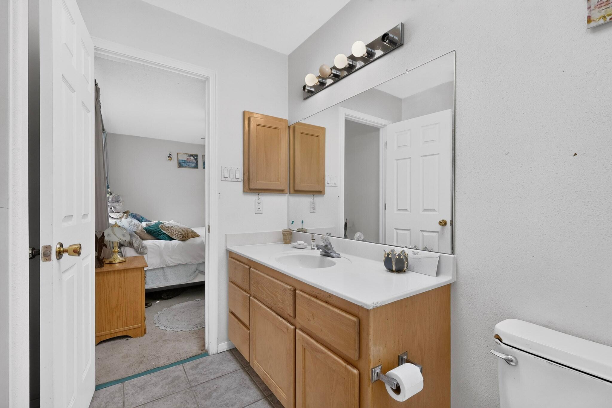 Bathroom with a wood vanity and large mirror, opening to a bedroom.