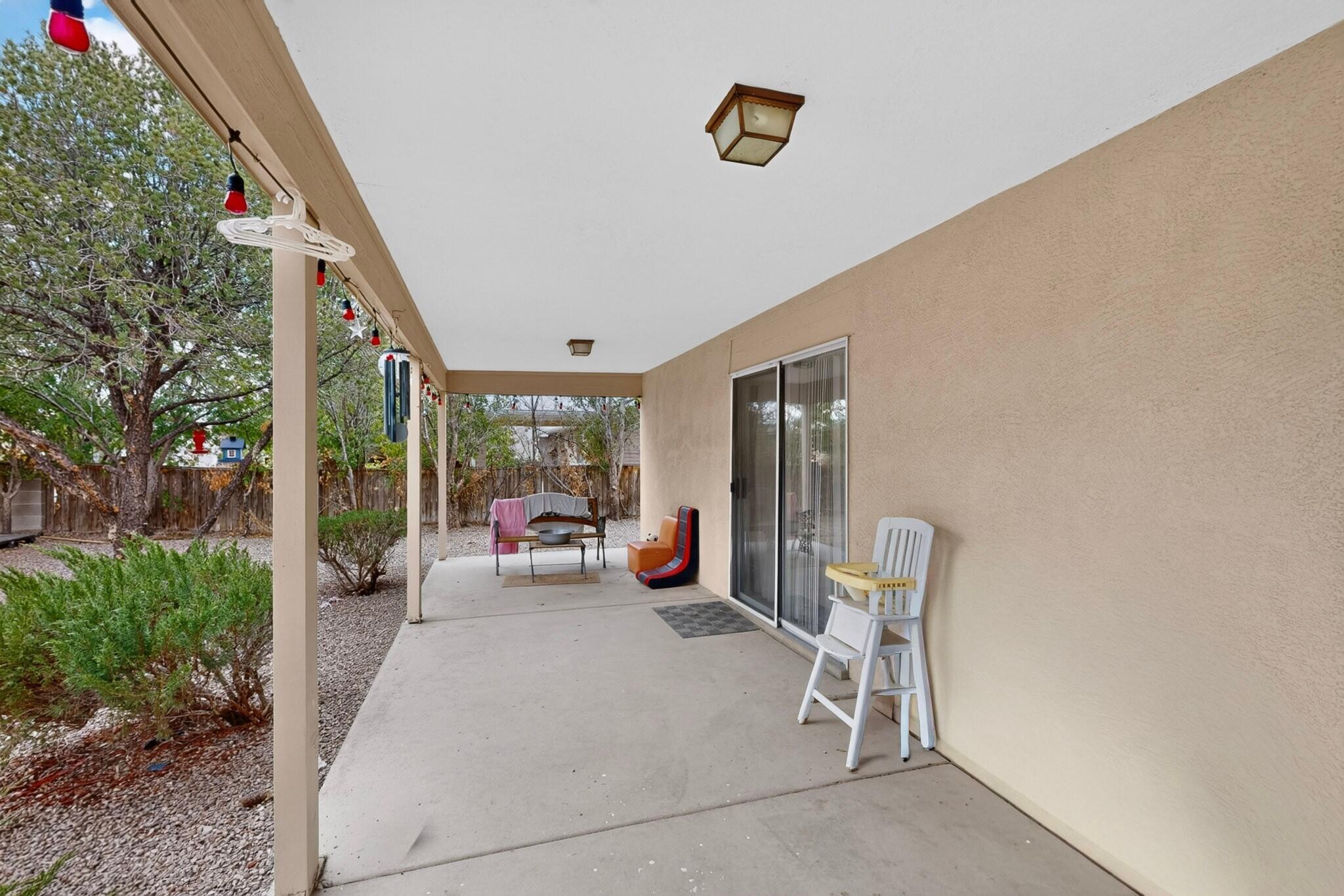 Covered concrete patio with outdoor seating, sliding glass door, and gravel yard.