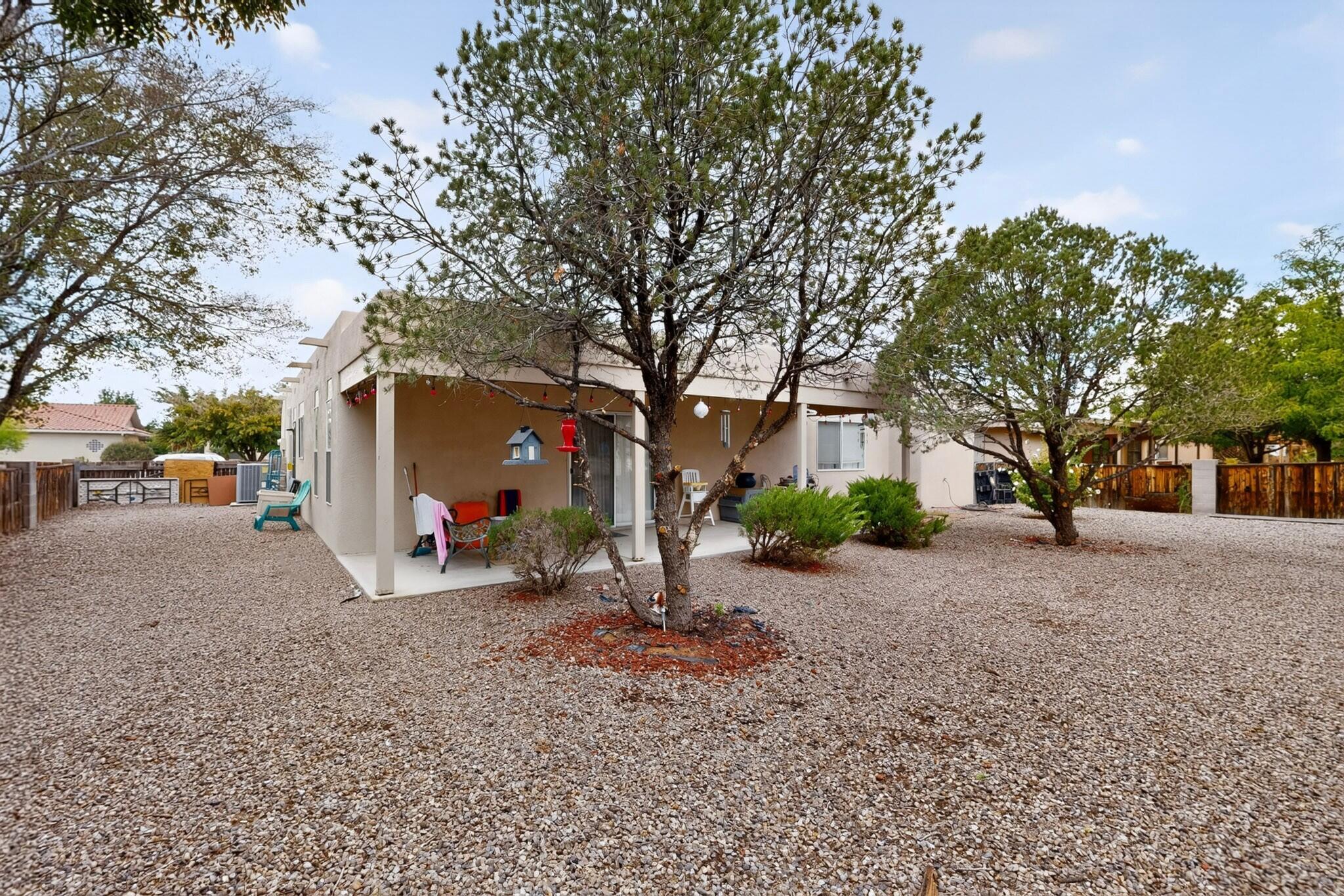 Home’s covered rear patio and spacious gravel yard with mature trees.