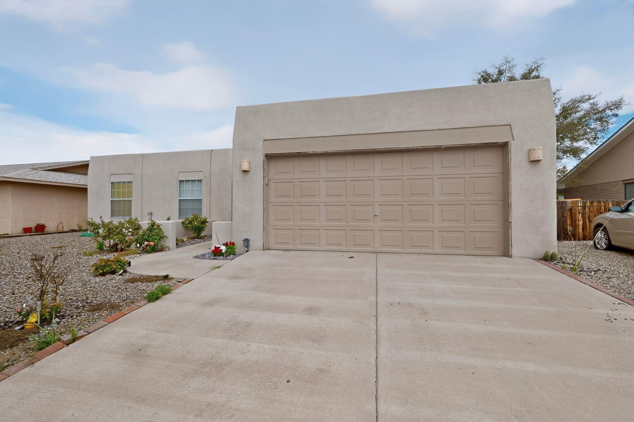 Stucco home with a large double garage door, broad driveway, and gravel landscaping.