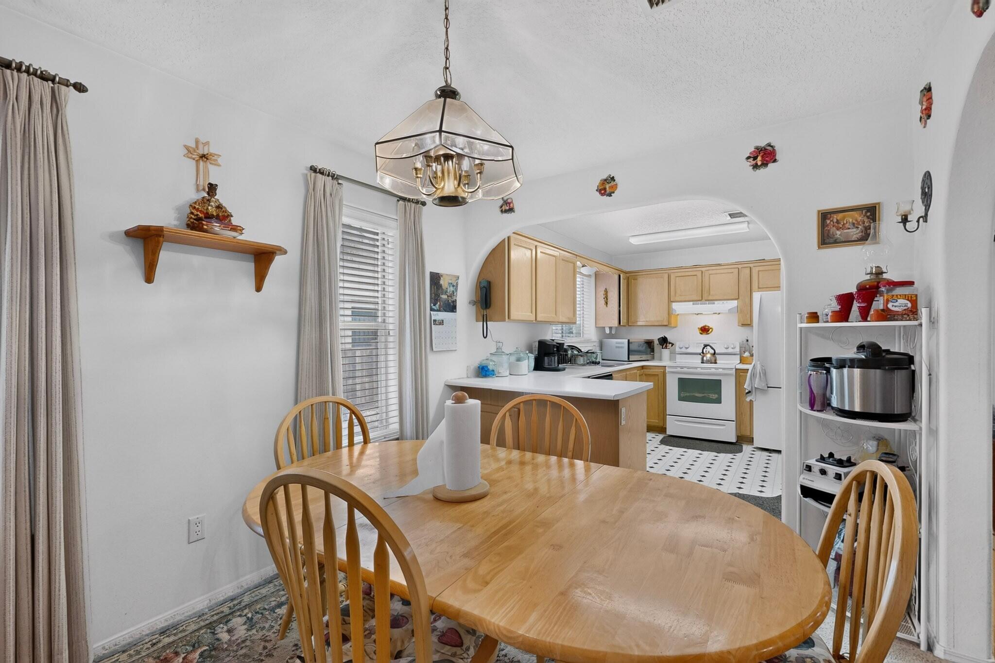 Dining area with a round wooden table opening into a kitchen with light wood cabinets and a central island.