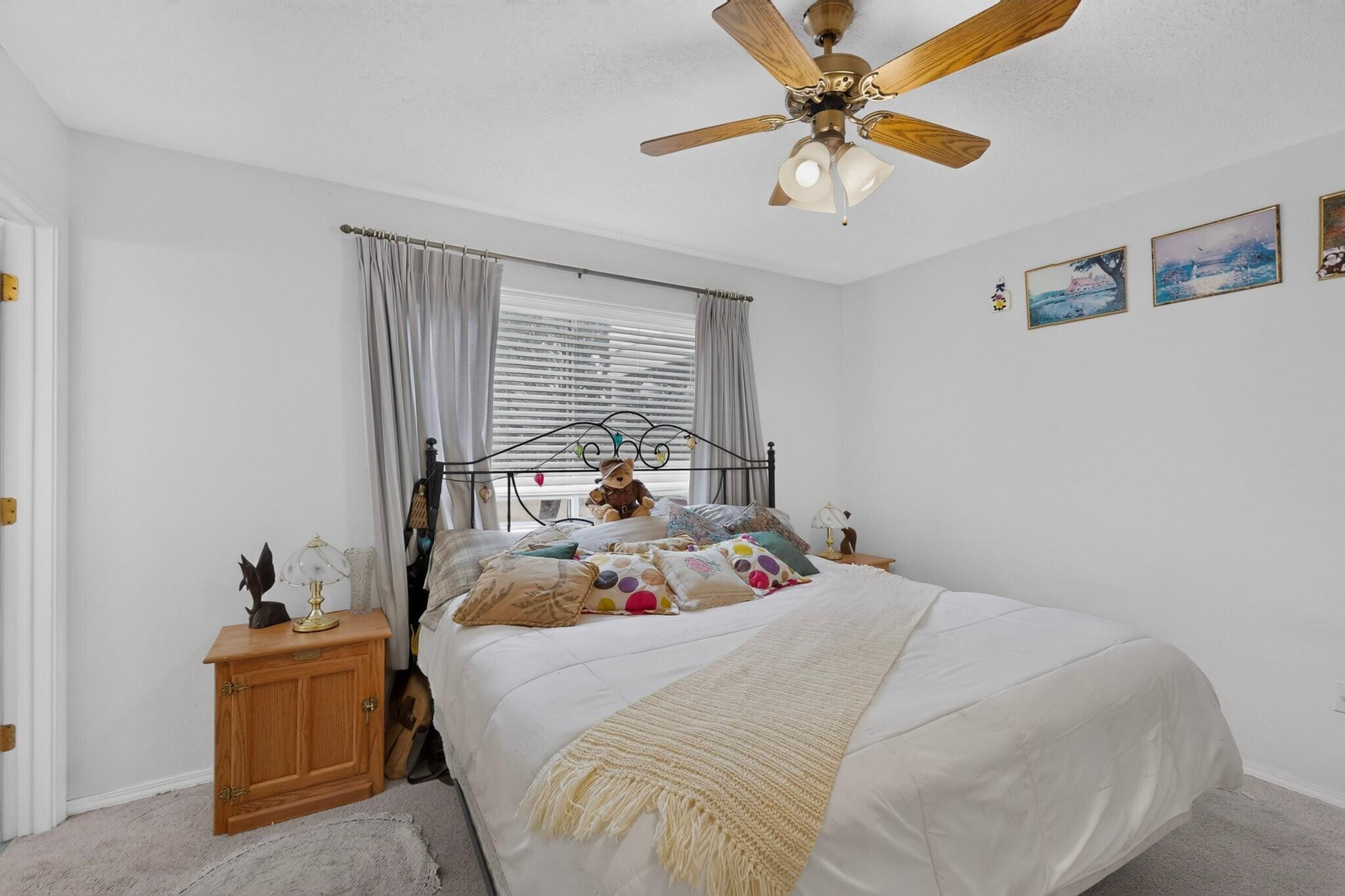Bedroom with a white bed, colorful pillows, wooden nightstand, and ceiling fan.
