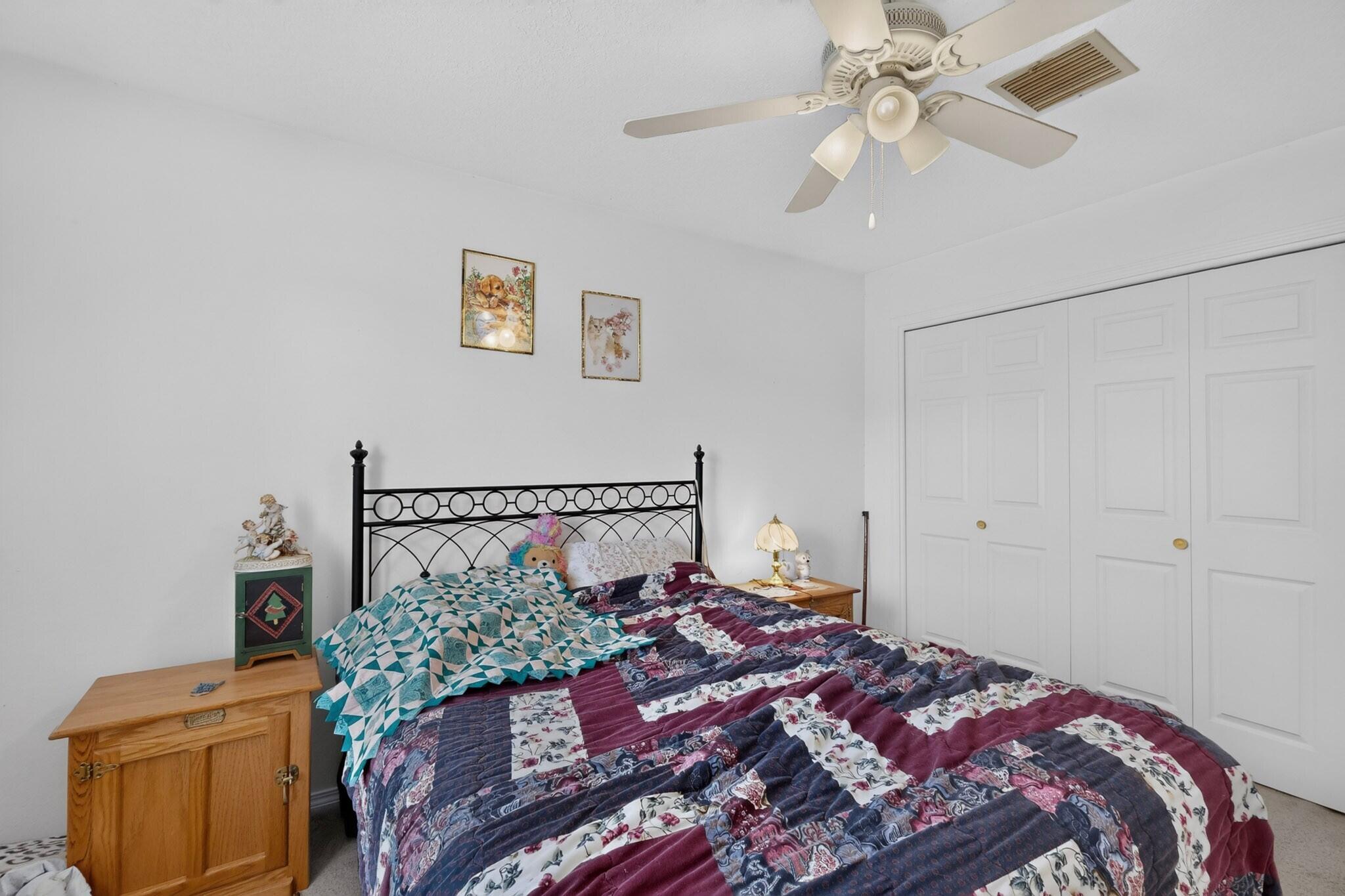 Bedroom with a black metal bed, colorful patchwork quilt, ceiling fan, and double closet doors.