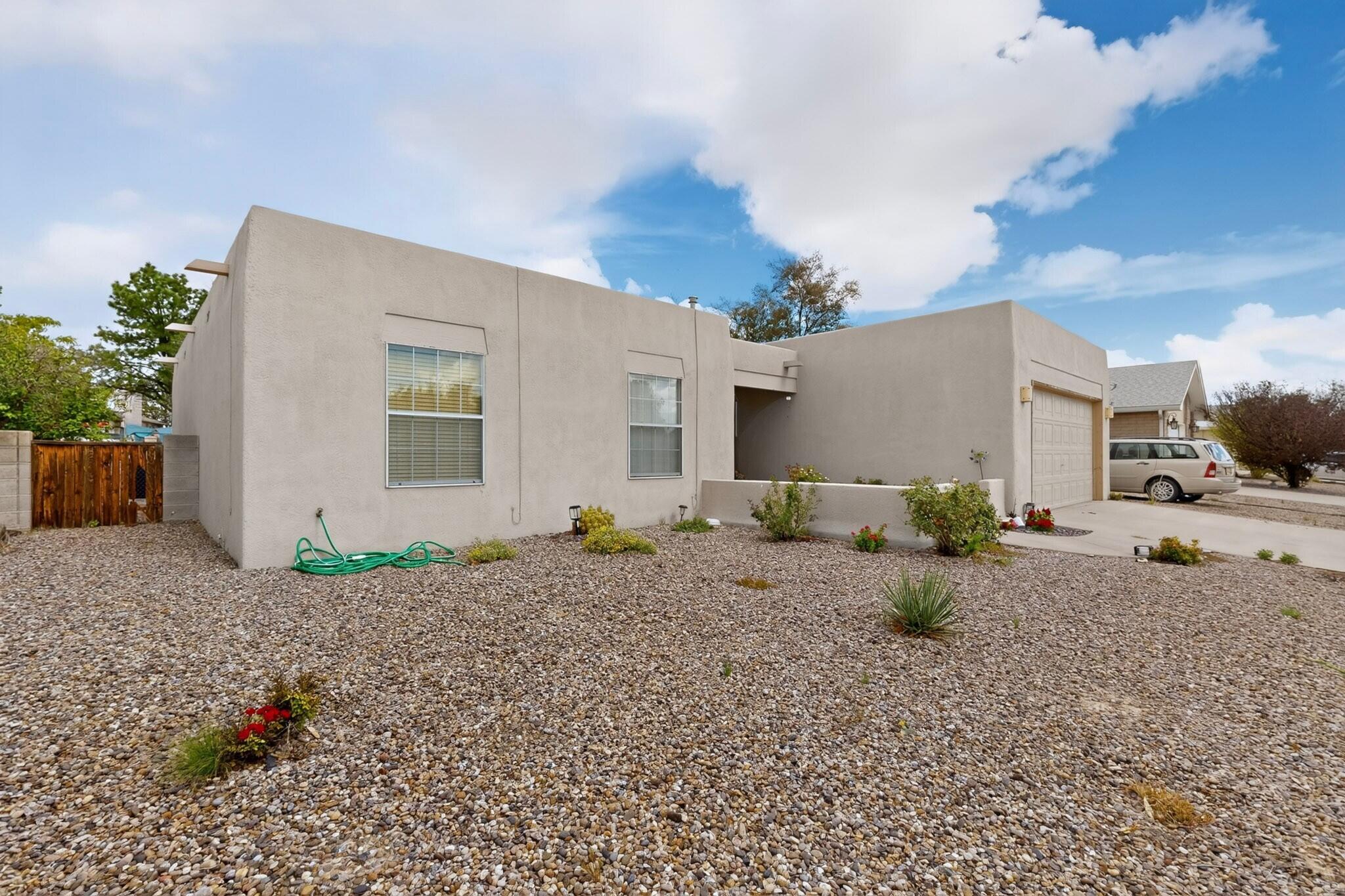 Single-story stucco home with a flat roof, attached garage, and gravel landscaping.