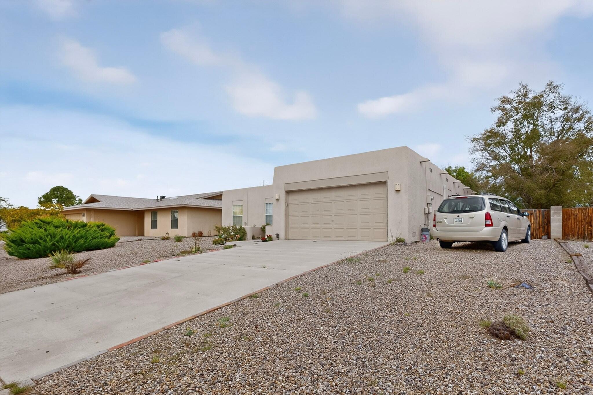 Single-story stucco home with an attached garage, wide driveway, and gravel landscaping.
