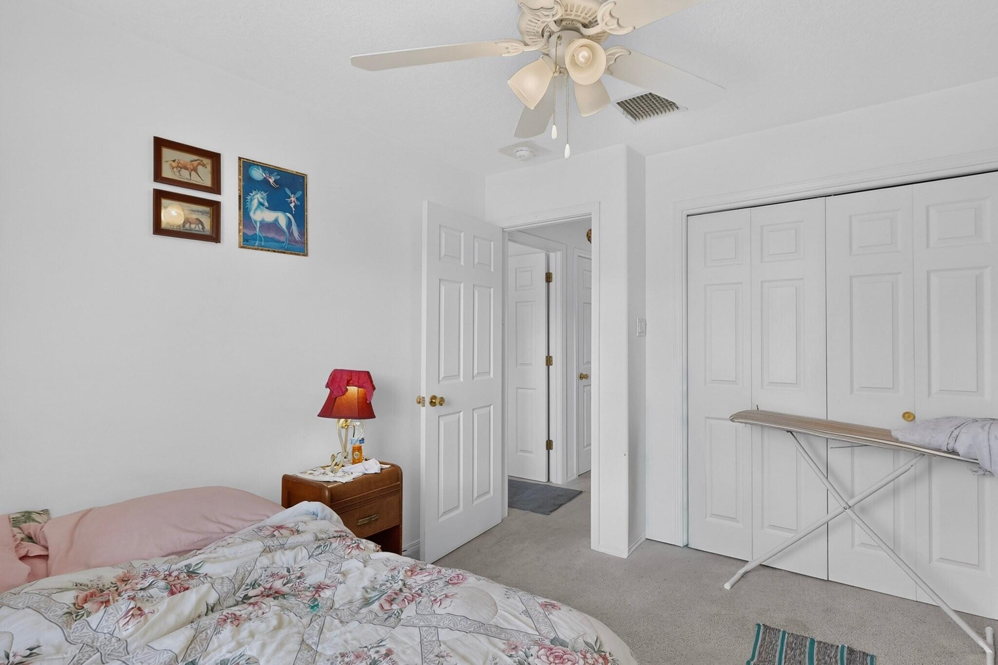 Bedroom with floral bedding, white paneled closets, and an ironing board.
