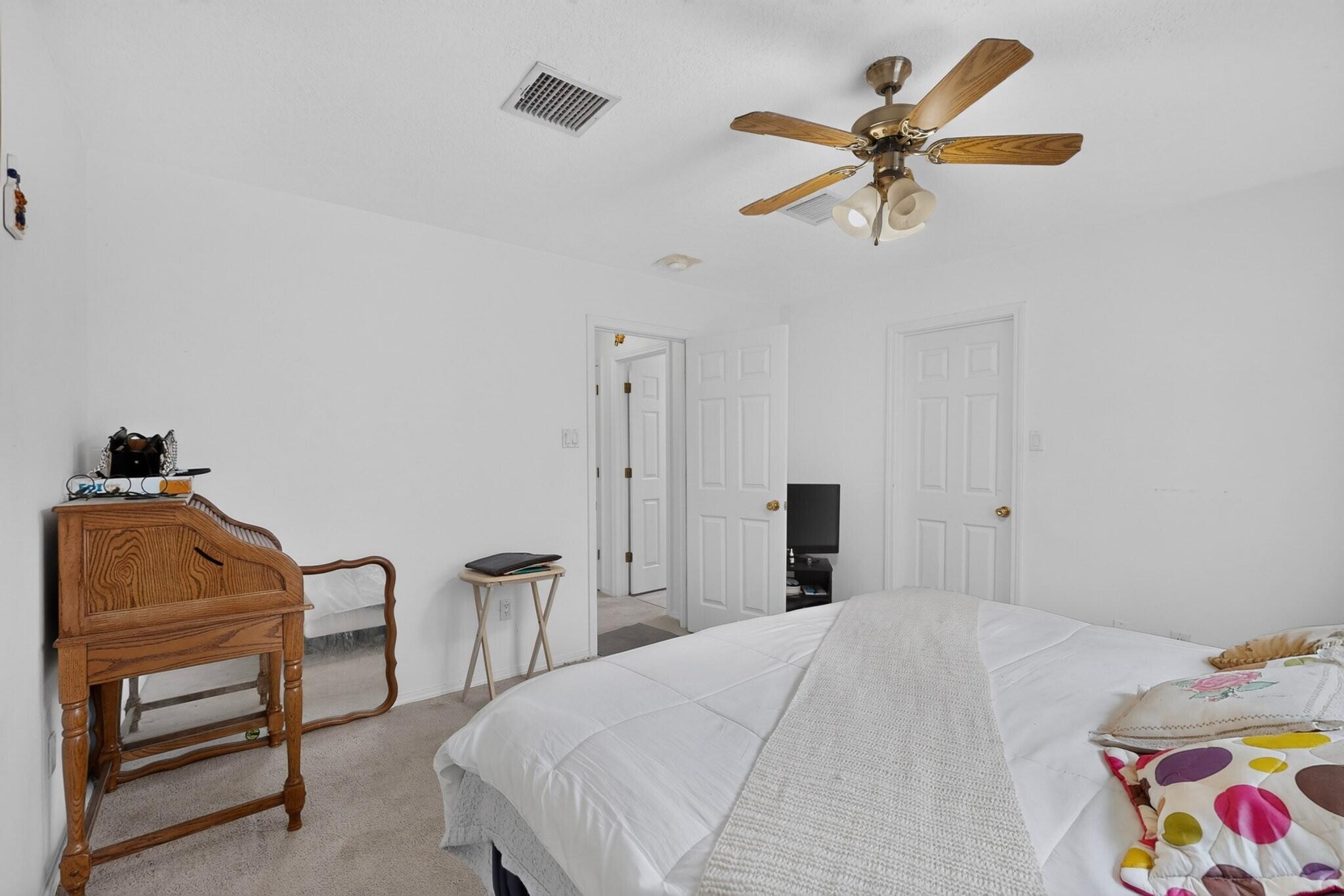 Bedroom with white bedding, colorful pillows, a wooden writing desk, and a ceiling fan.