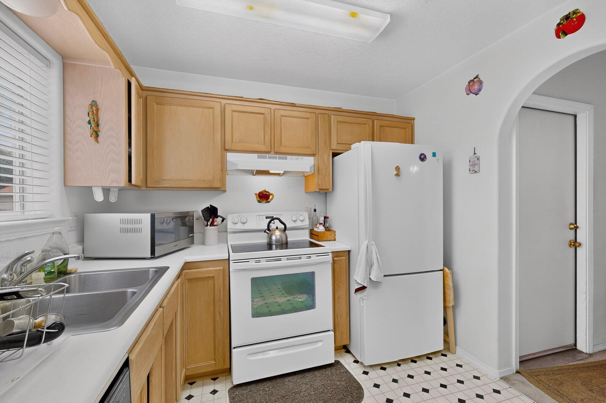 Kitchen with light wood cabinets, white appliances, a double sink, and black-and-white tiled floor.