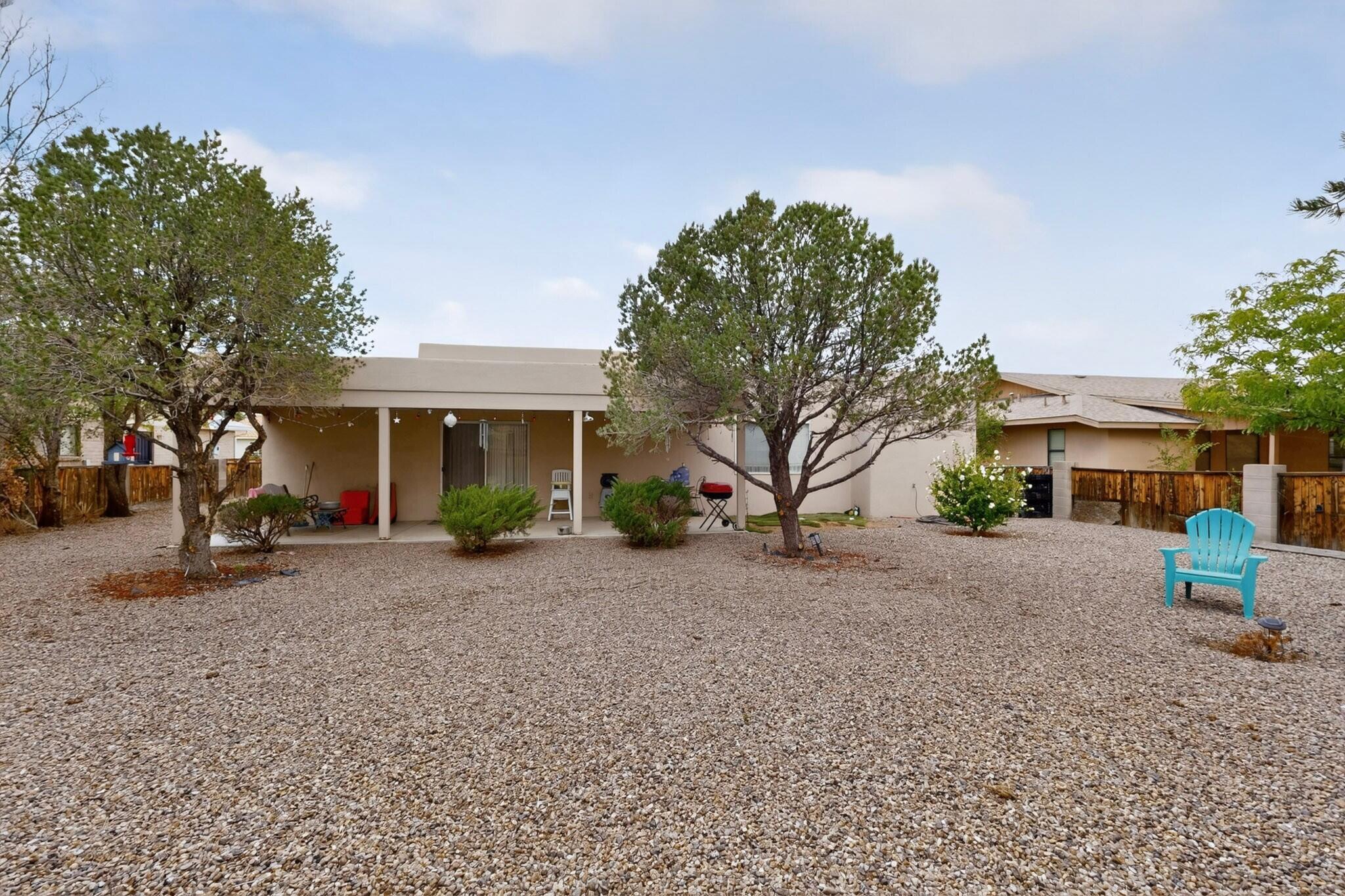 Home’s gravel backyard with a covered patio, mature trees, and a turquoise Adirondack chair.