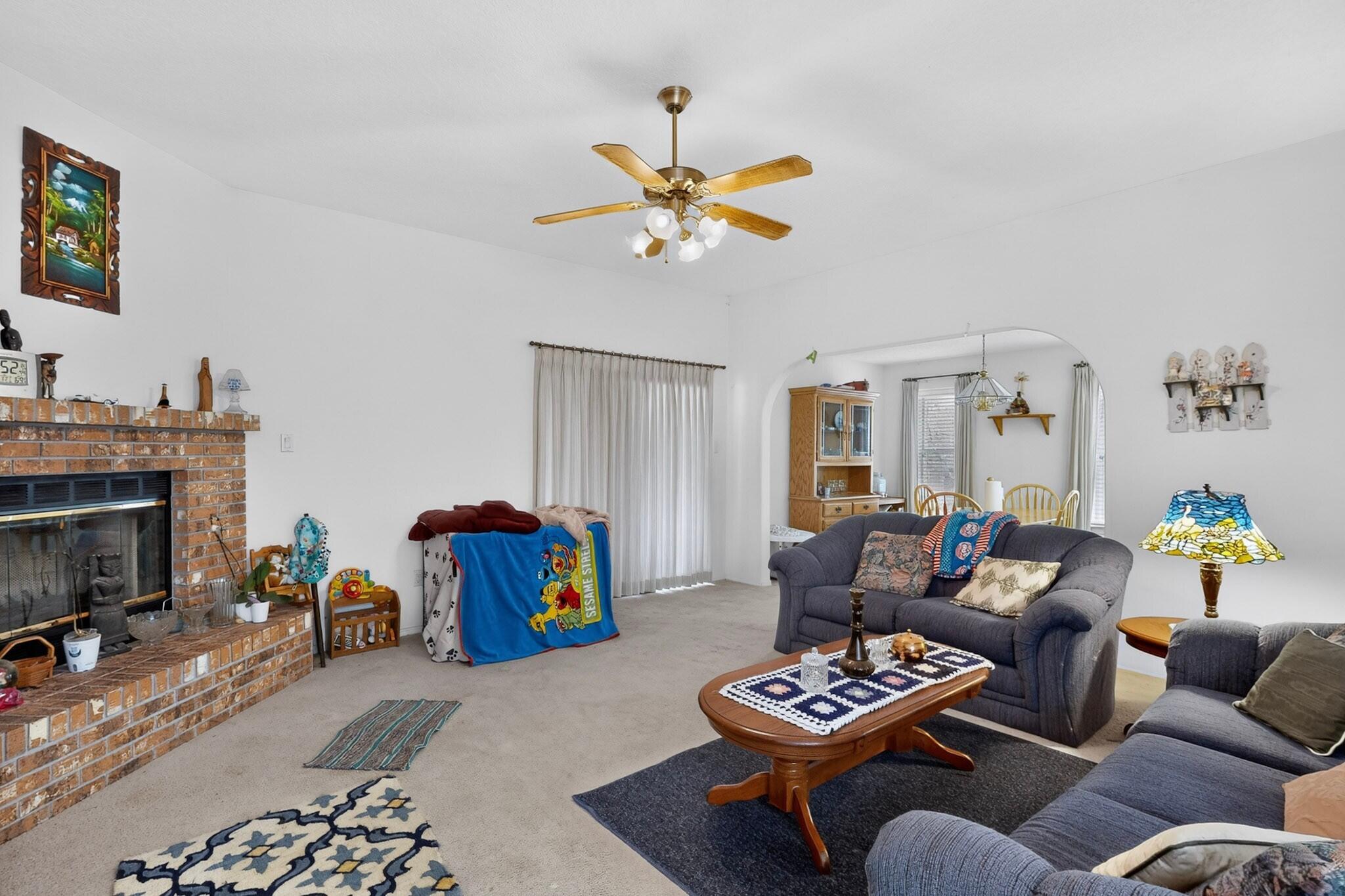 Living room with a brick fireplace, gray sofas, and an arched opening to the dining area.