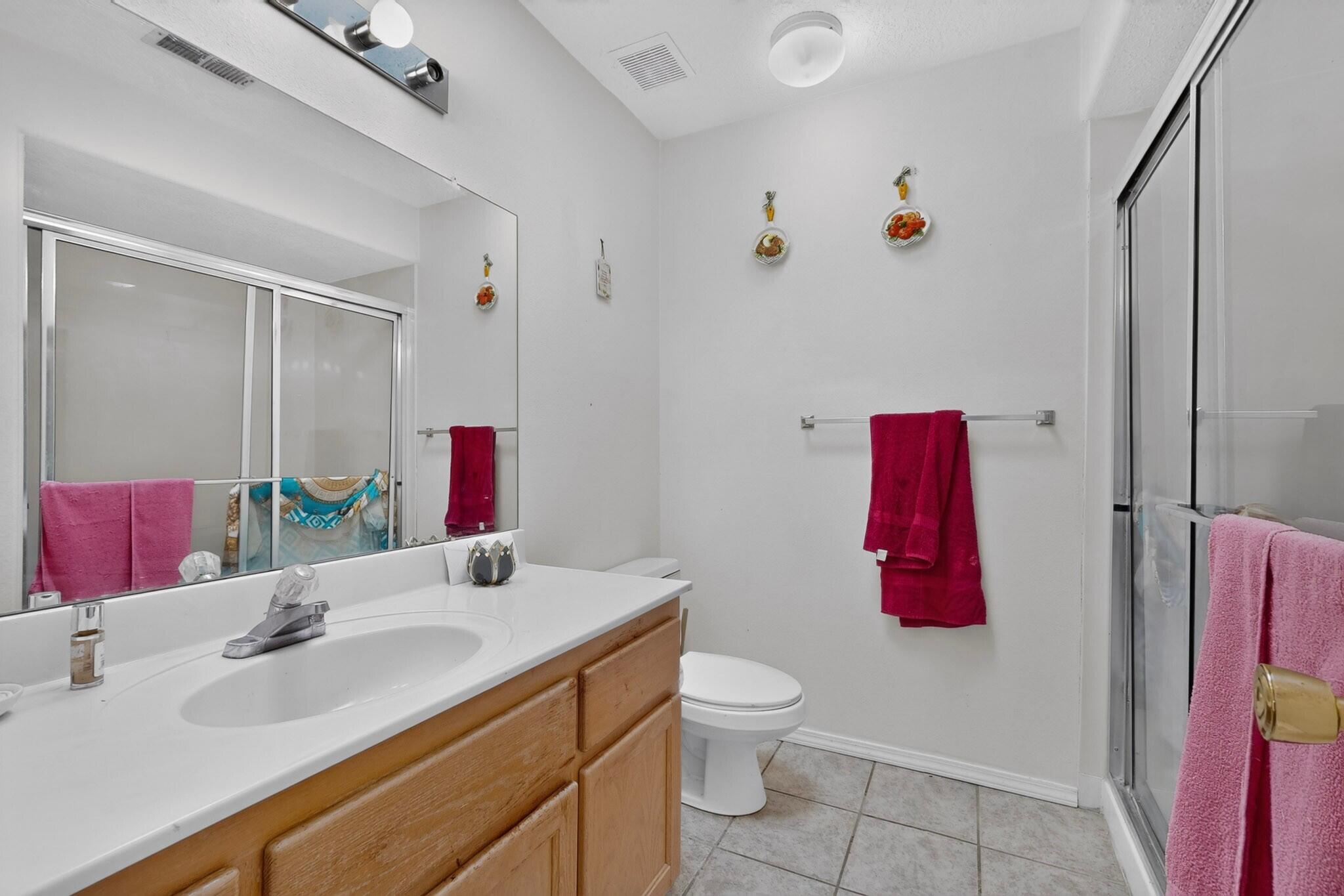 Bathroom with a wood vanity, large mirror, toilet, and glass shower enclosure.