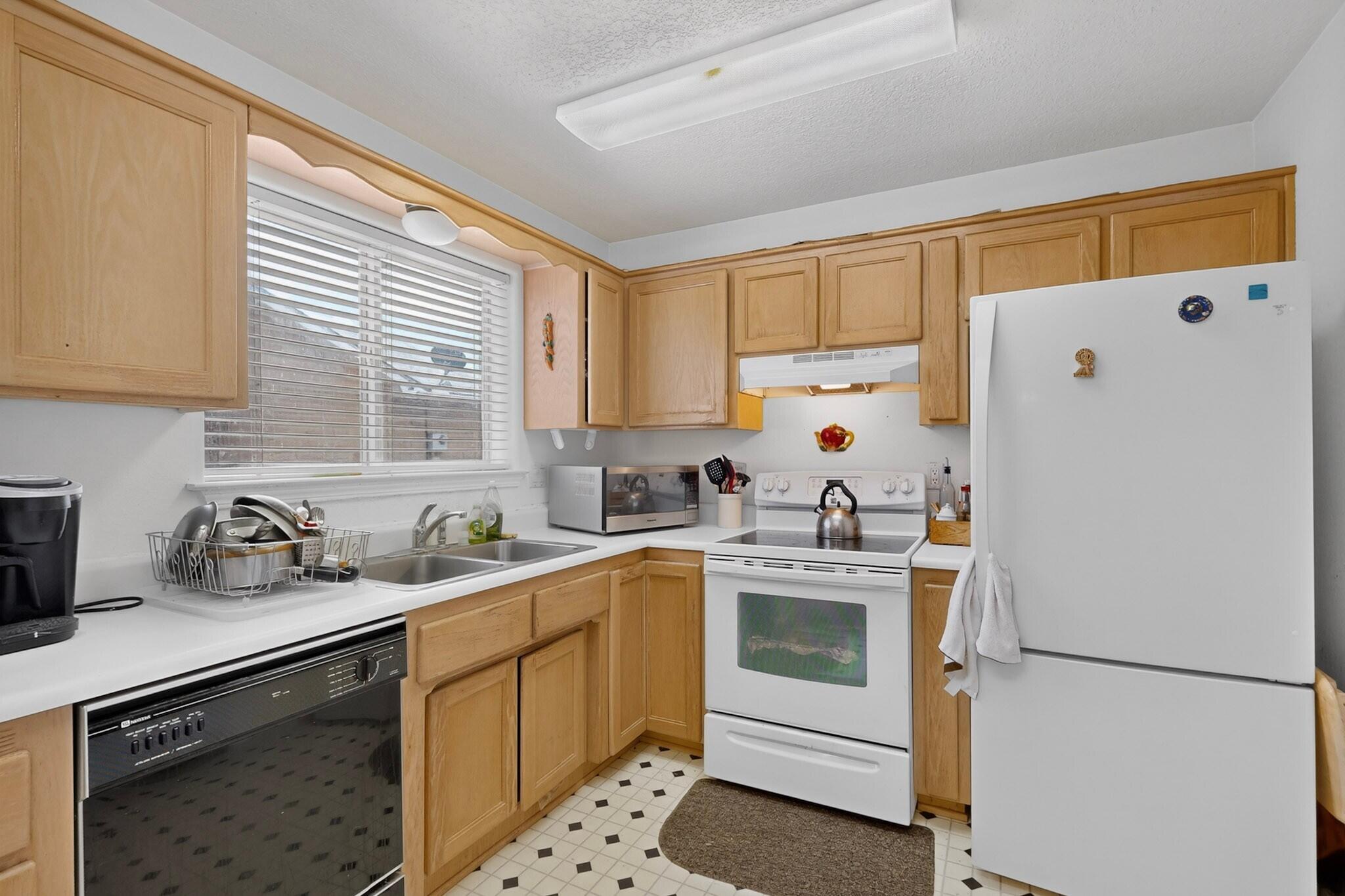 Kitchen with light wood cabinets, white appliances, and a double sink beneath a window.