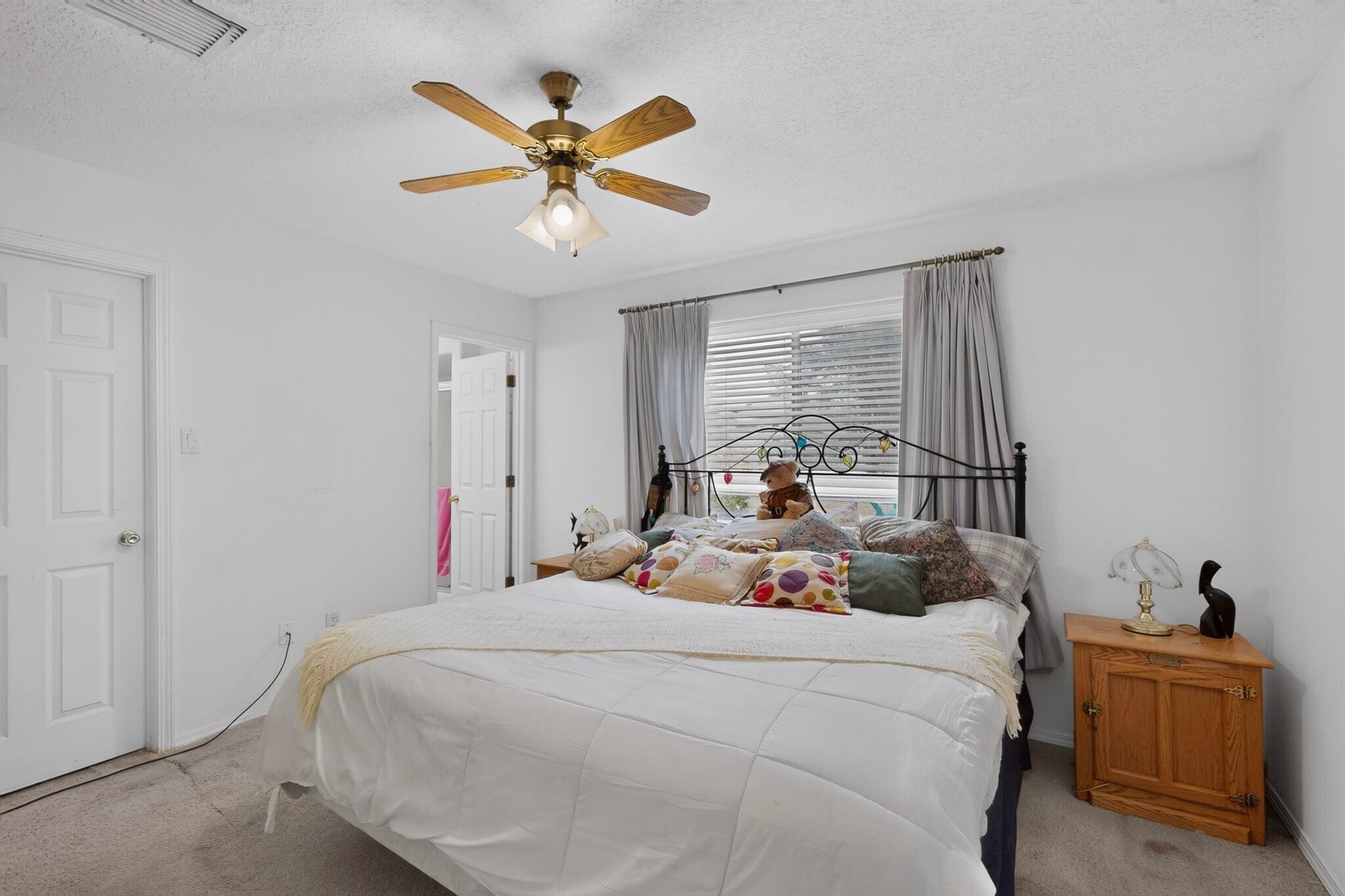 Bedroom with a large white bed, colorful pillows, and a wooden ceiling fan.