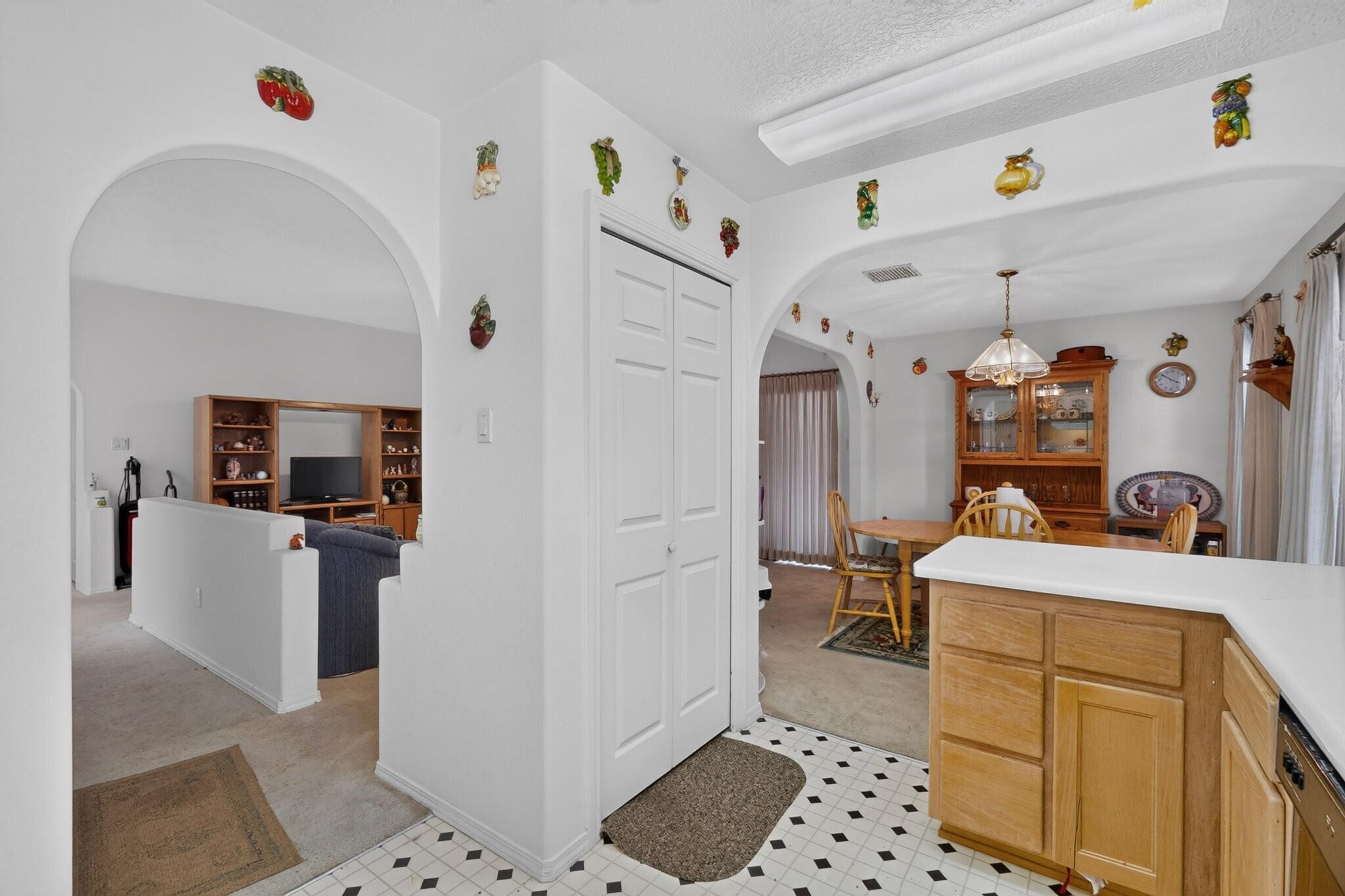 Kitchen opening to a dining room and living room, with arched openings and colorful fruit wall decorations.